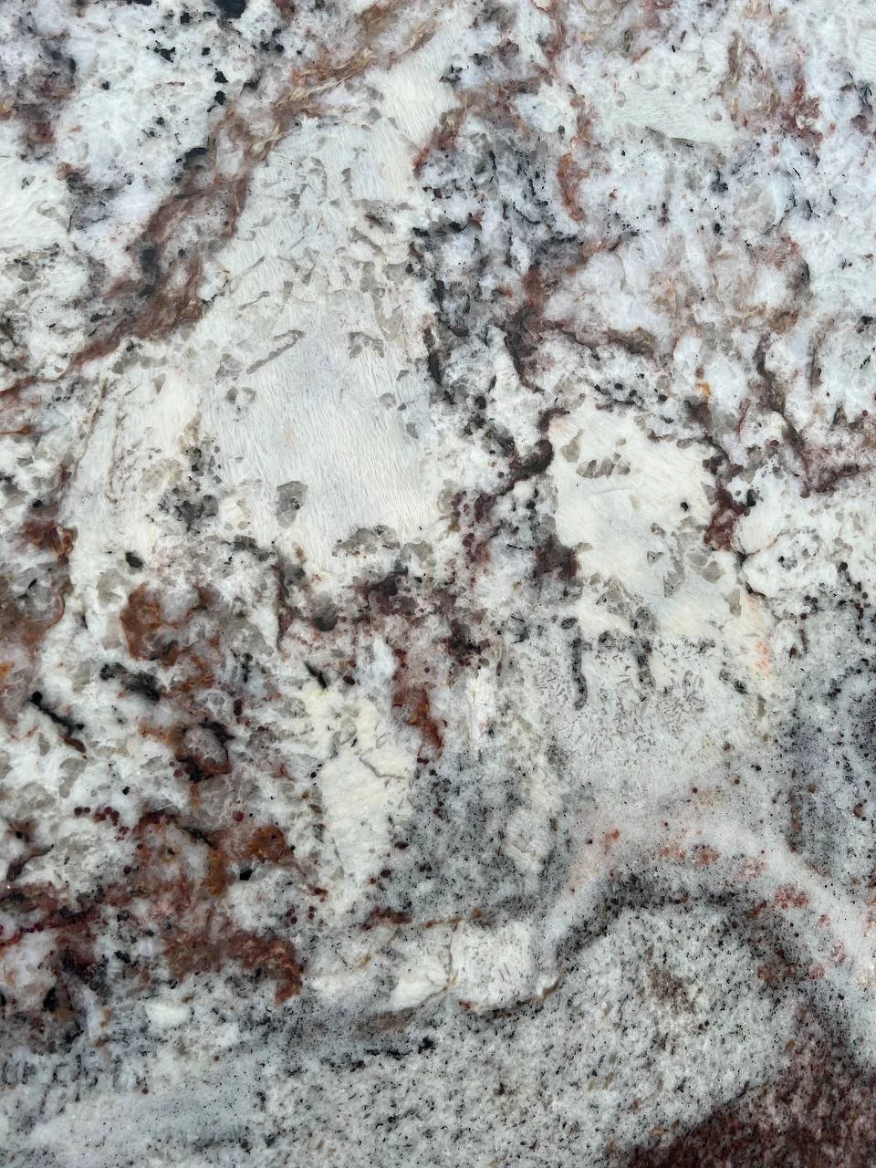 White Spring Granite. A Close-up of a granite slab with a mix of white, gray, and brown colors and a speckled texture.