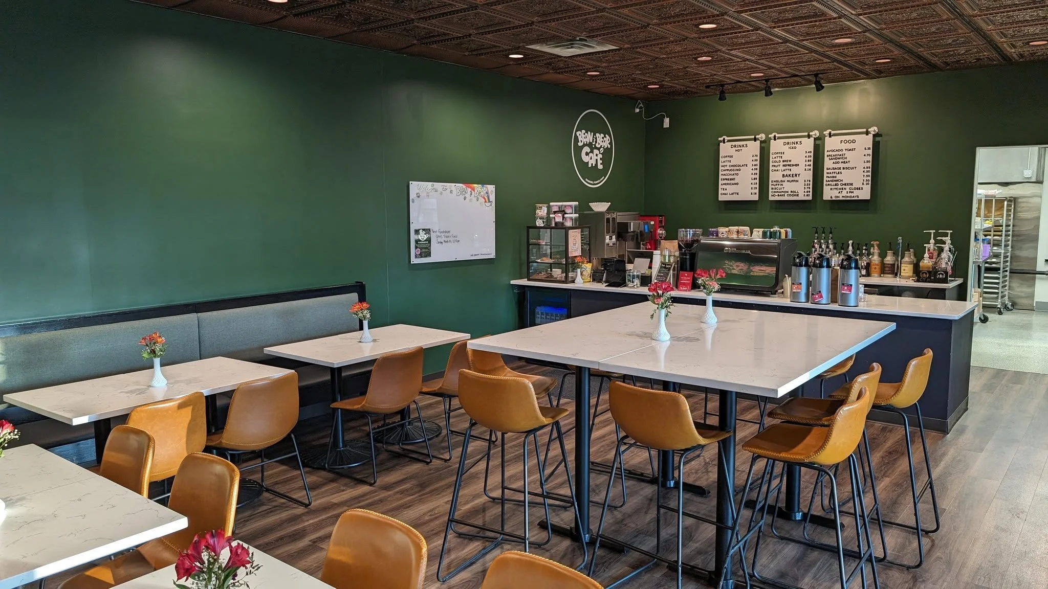 Interior of a modern cafe with green walls, high tables, brown leather chairs, decorative ceiling, and a counter with drinks menu.