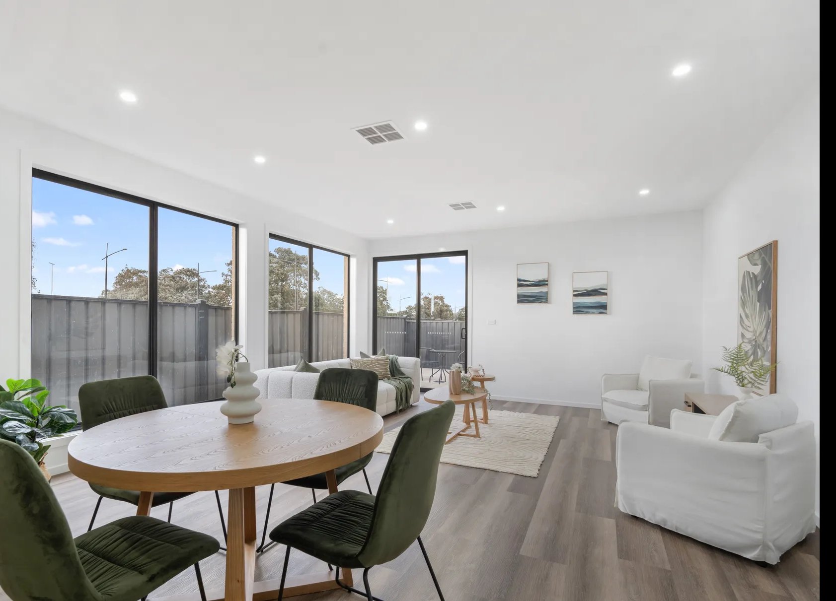 Bright living room with large windows, white walls, modern furniture, and framed artwork.