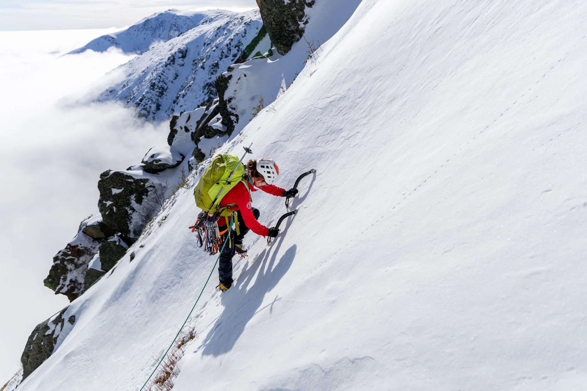 Climber with ice tools on a steep snow slope above the clouds on Mount Washington, New Hampshire