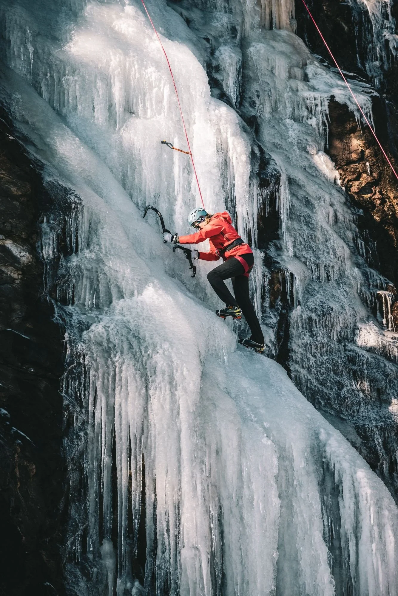 Climber in a red jacket learning to ice climb on top-rope at Highway 215 ice near Brevard, North Carolina