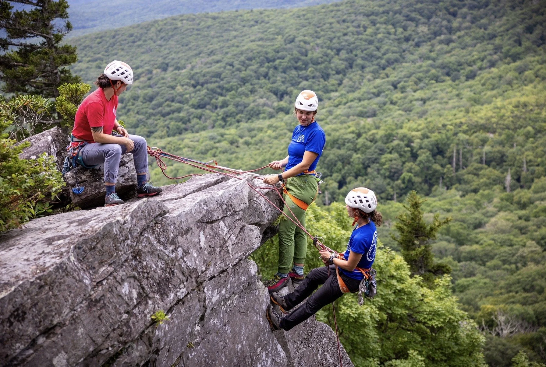 Girls rock climbing. AMGA single pitch instructors practicing a belayed rappelling setup. Mountains are in the background.