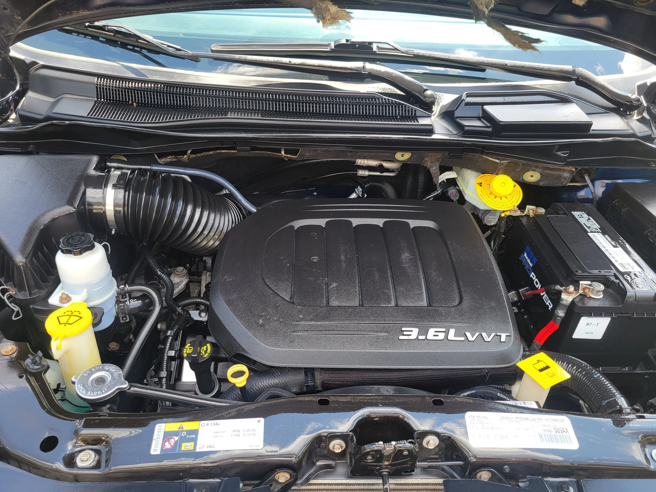 A car engine bay with various components, including a 3.6L V6 engine, yellow oil cap, windshield washer fluid container, and other engine parts.