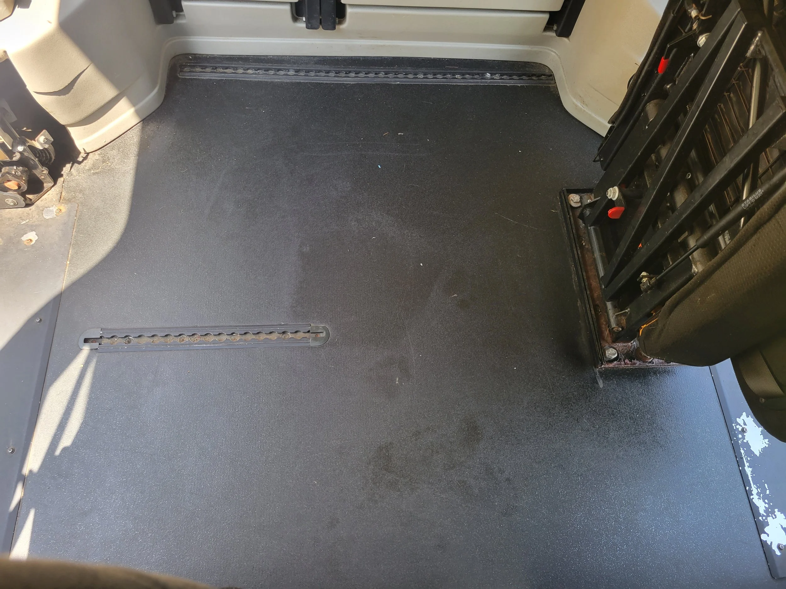 Close-up view of a vehicle interior floor with black carpet, a metal adjustment track, and part of the seat frame on the right side.