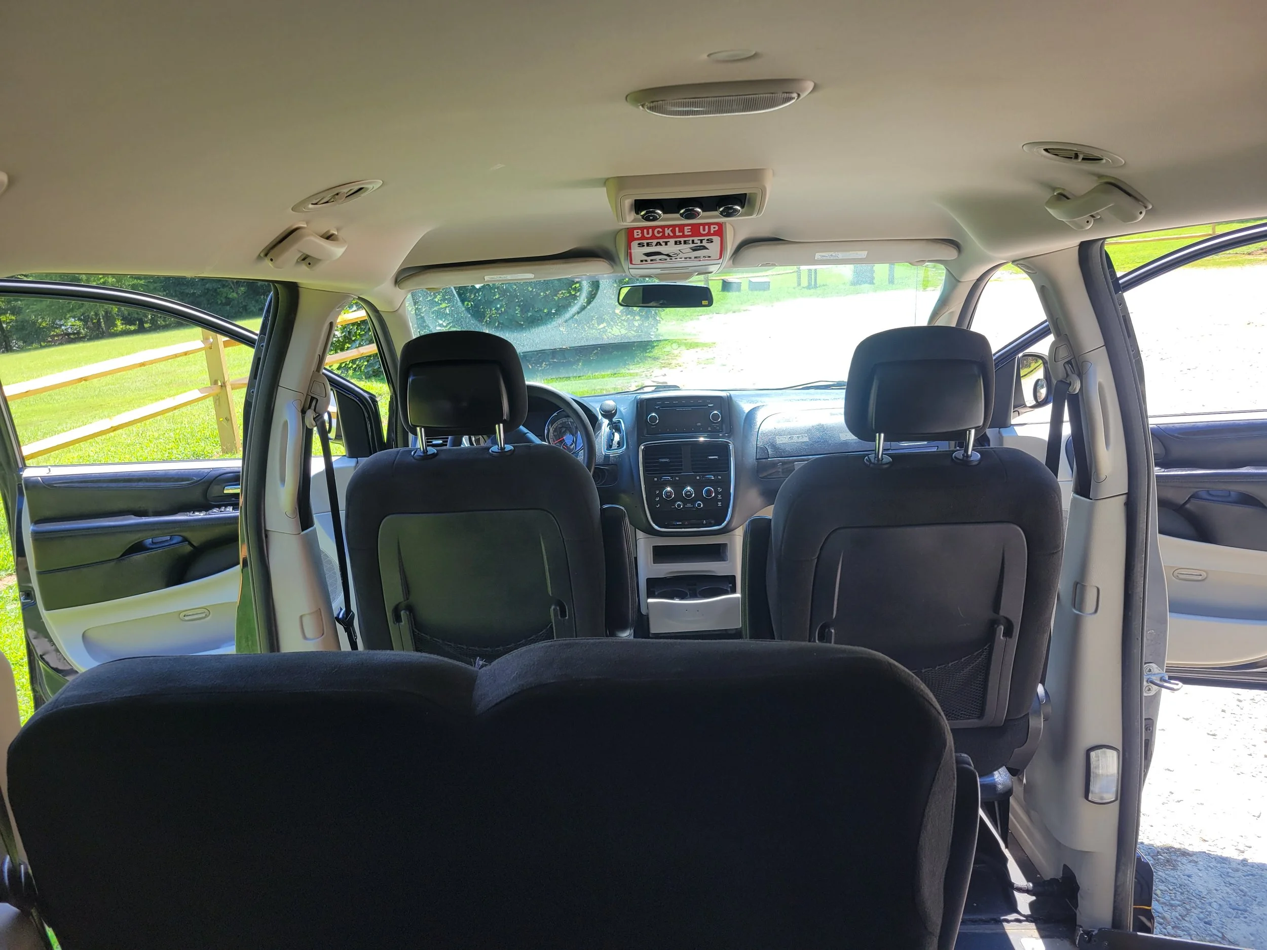 View of the interior of a vehicle showing the front seats, dashboard, and ceiling. The ceiling has a sign that says 'Buckle Up Seat Belts'.