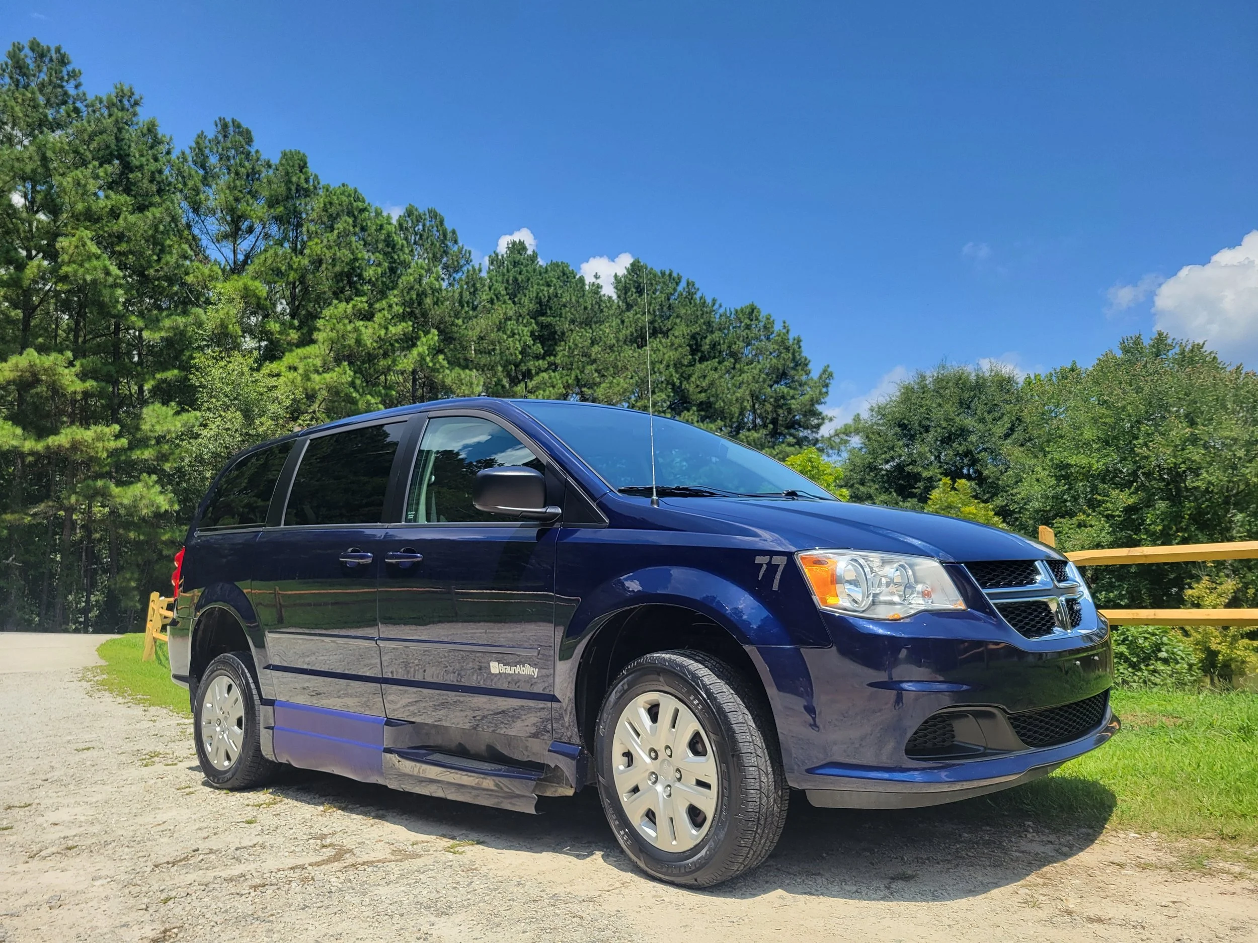A blue minivan parked outdoors with green trees and a blue sky in the background.