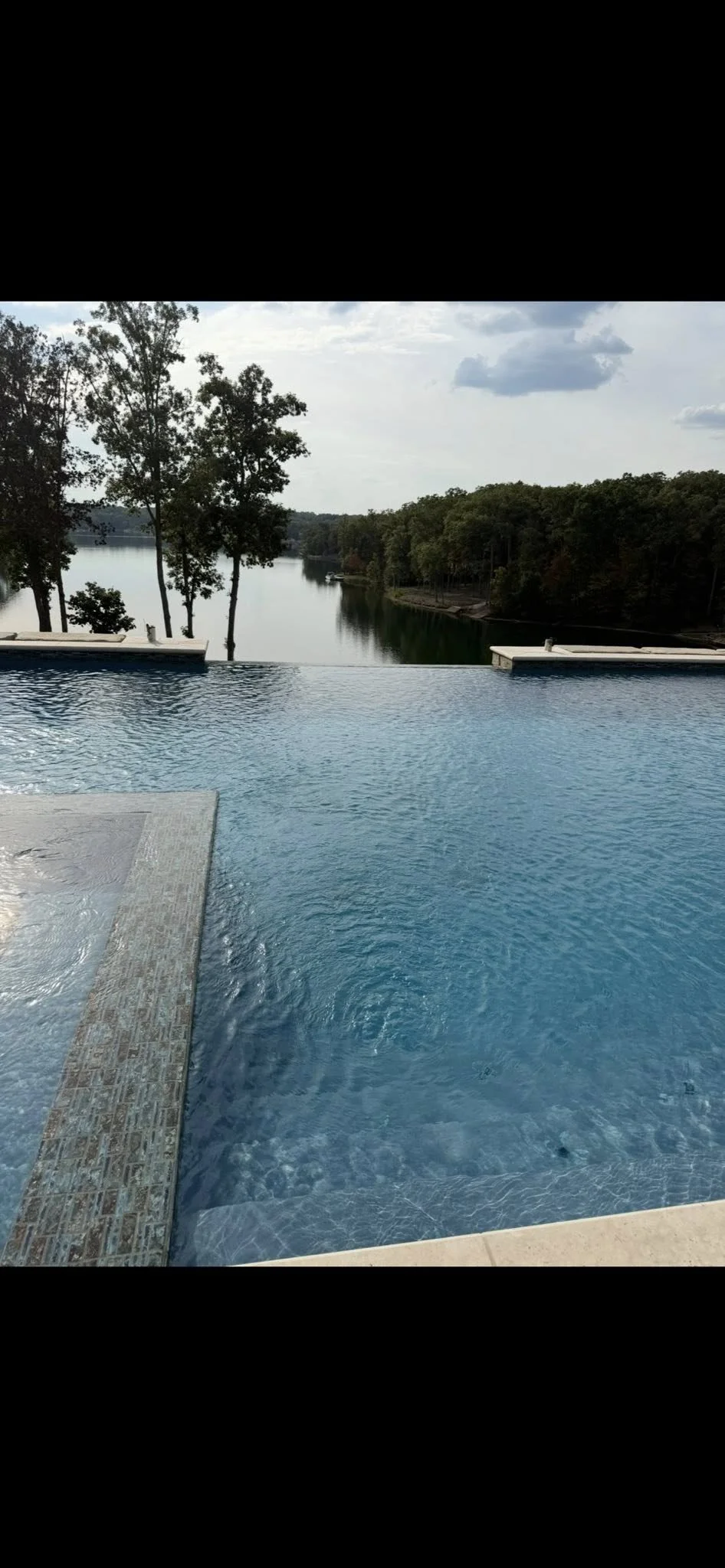Infinity pool overlooking a river with trees and cloudy sky in the background.