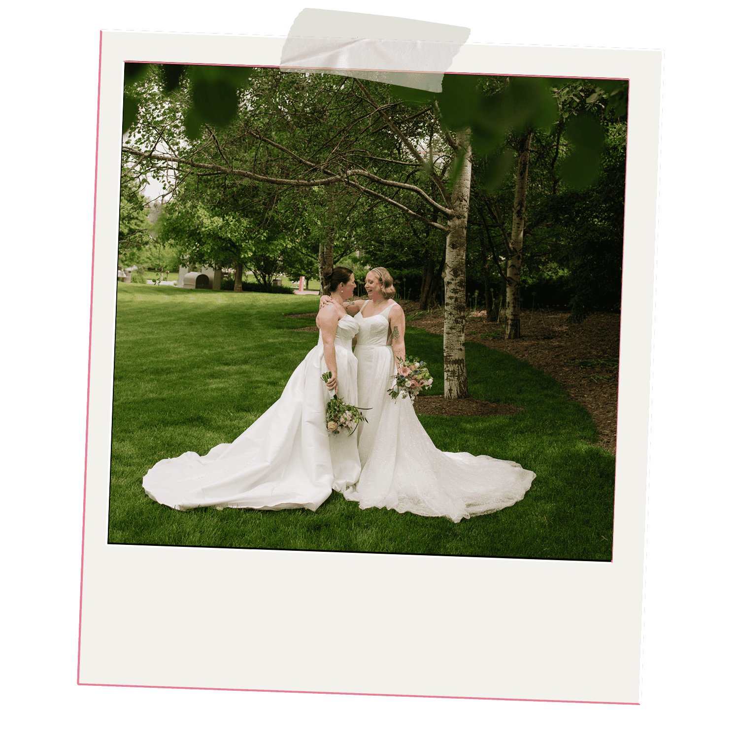Two brides in wedding dresses sharing a moment outdoors in a green park with trees and grass, holding bouquets.