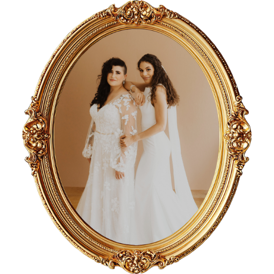 Two women in wedding dresses posing together inside an ornate gold oval frame.