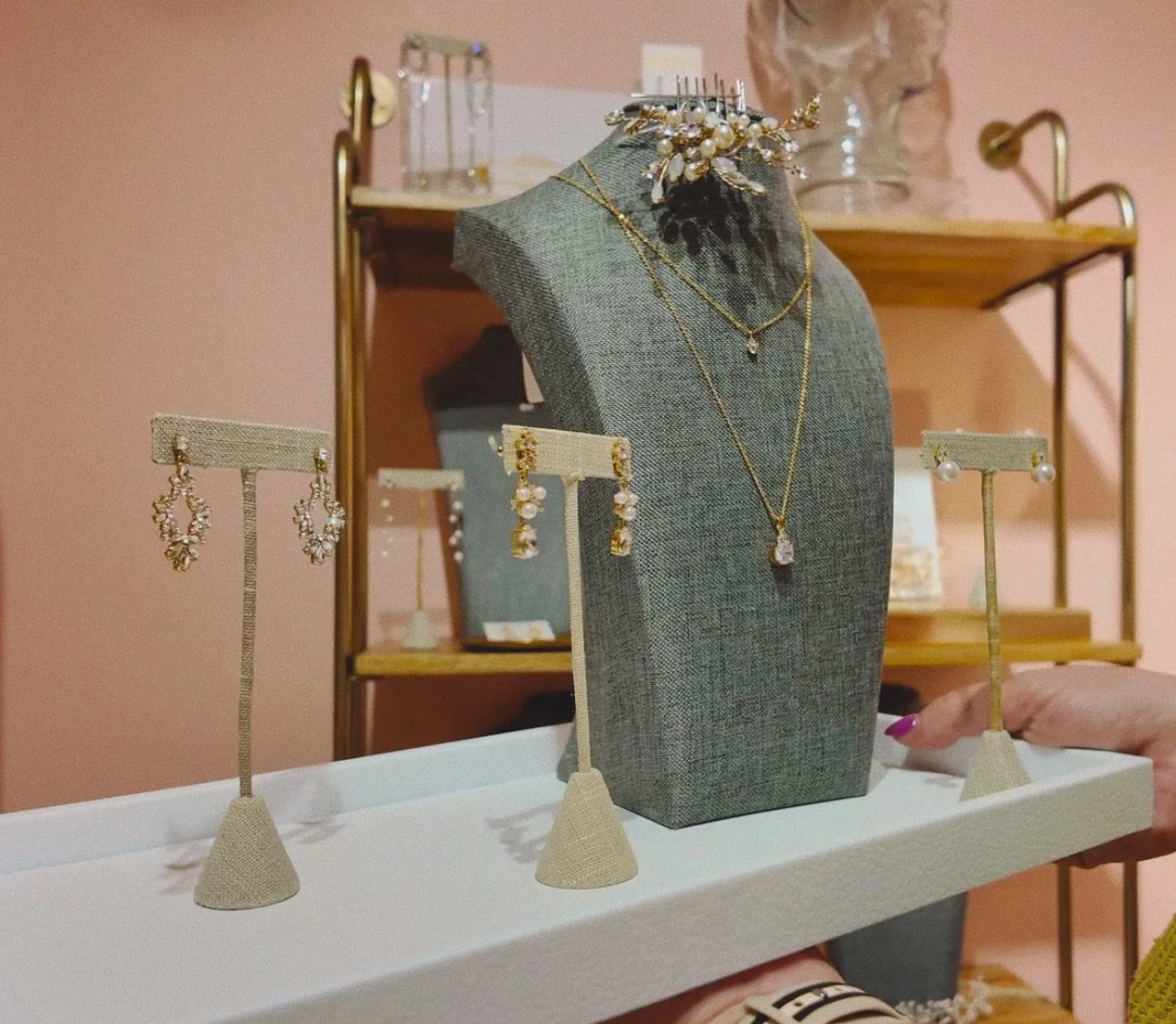 Jewelry display featuring earrings and necklaces on a gray bust and stands, with a shelf in the background.