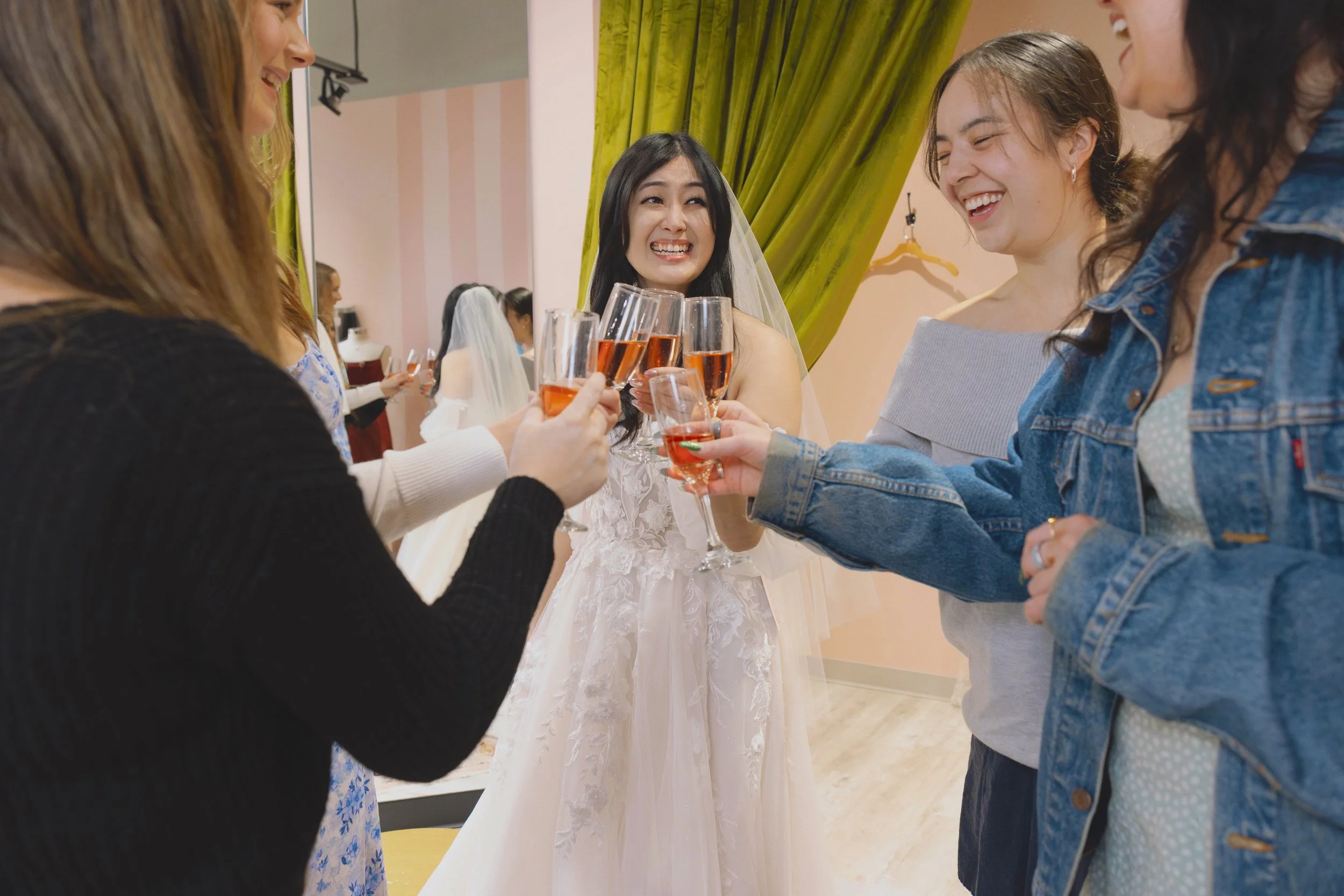Group of women, one in a wedding dress, celebrating a Yes moment with a champagne toast during a bridal appointment.
