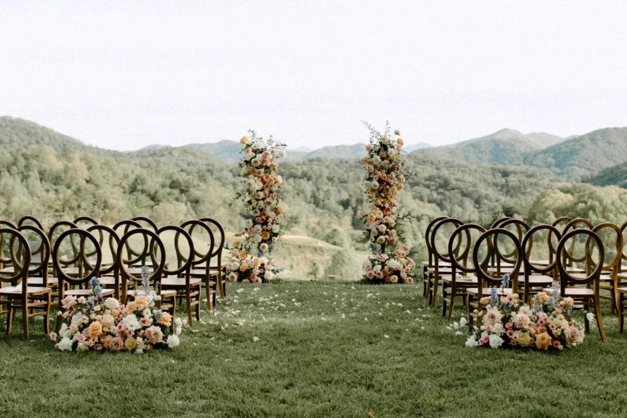 Outdoor wedding ceremony setup with chairs, floral arrangements, and an arch in a scenic mountain setting.