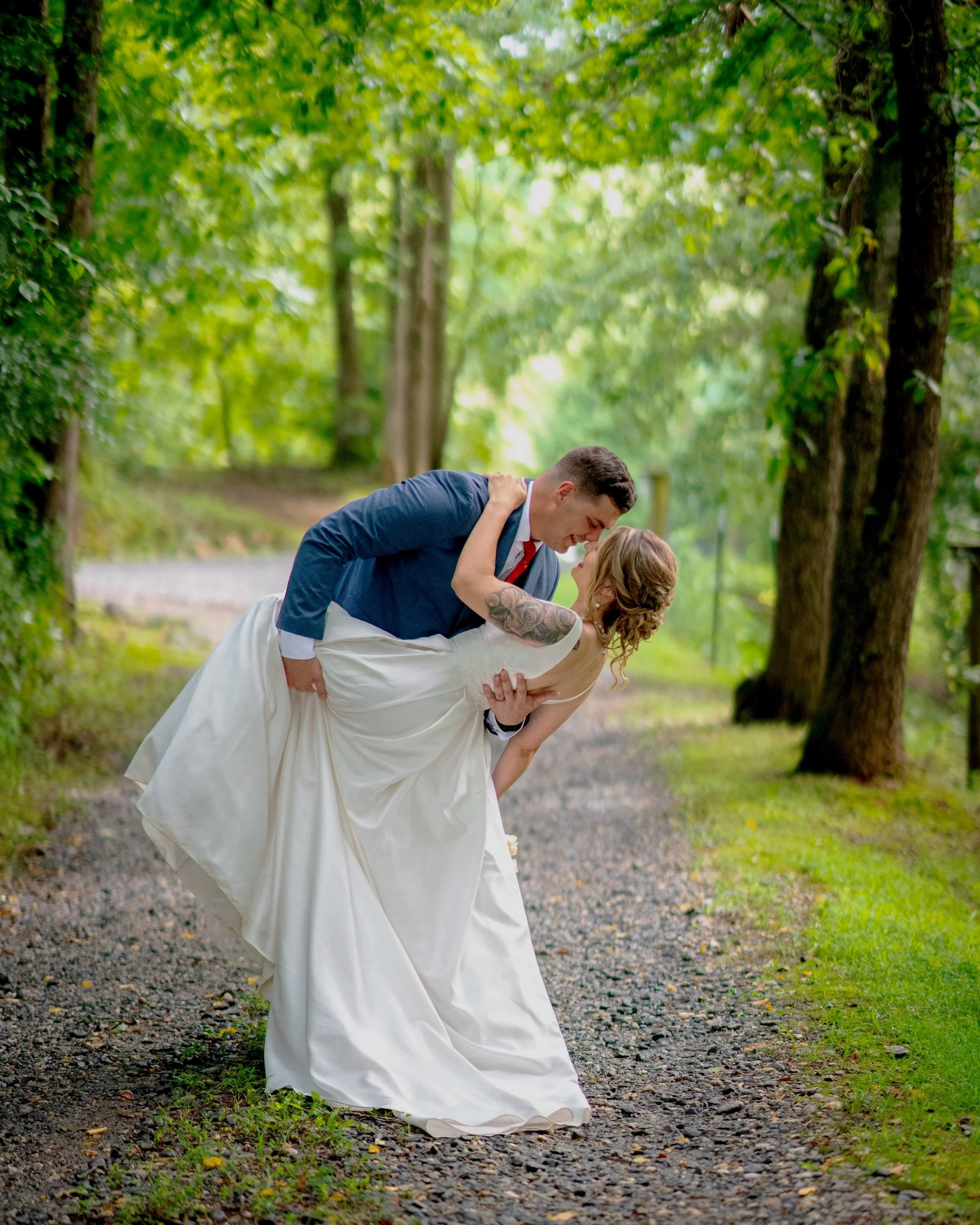 A bride and groom in a wooded outdoor setting, with the groom dipping the bride as they look at each other.