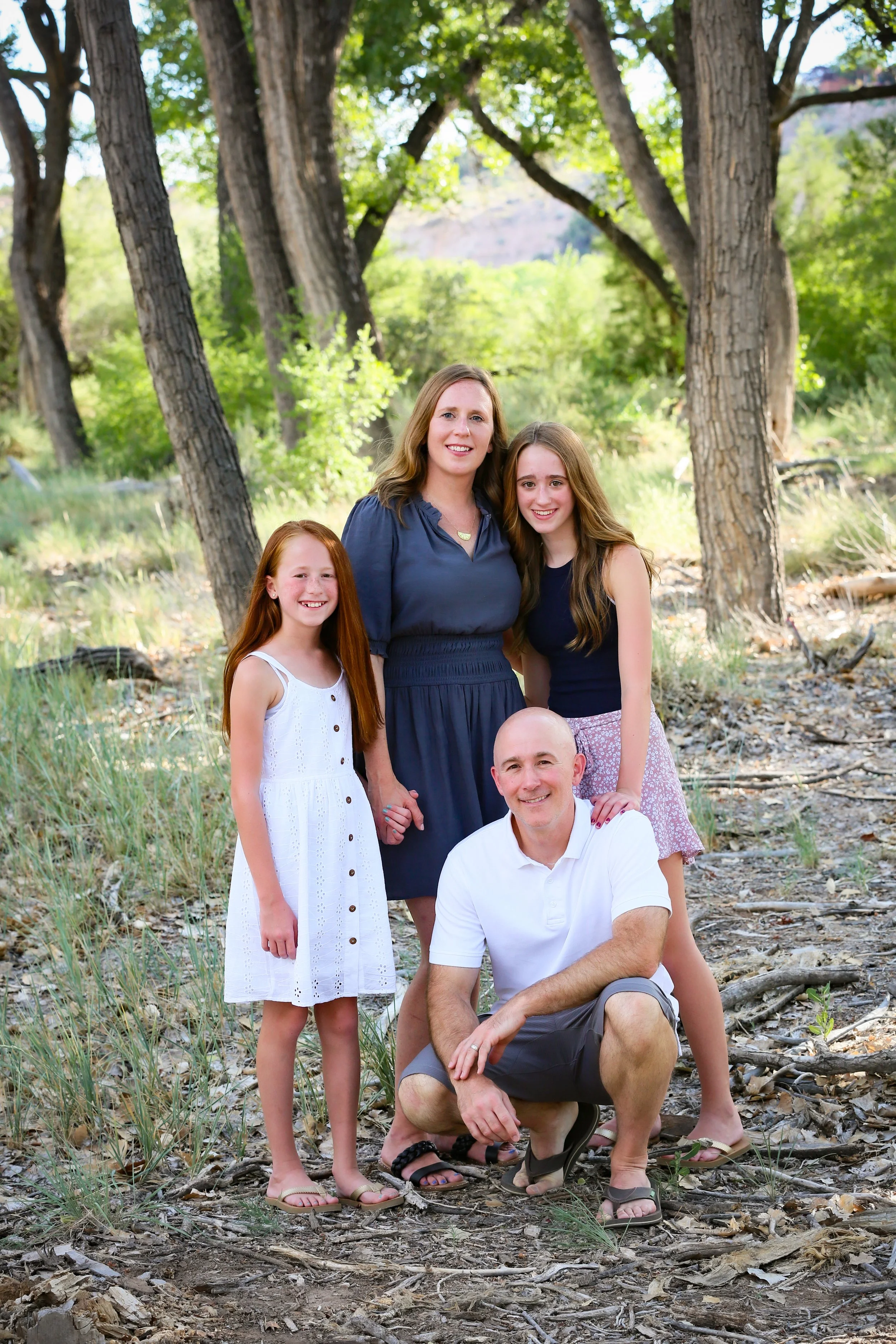 A family of five standing outdoors among trees, smiling at the camera.