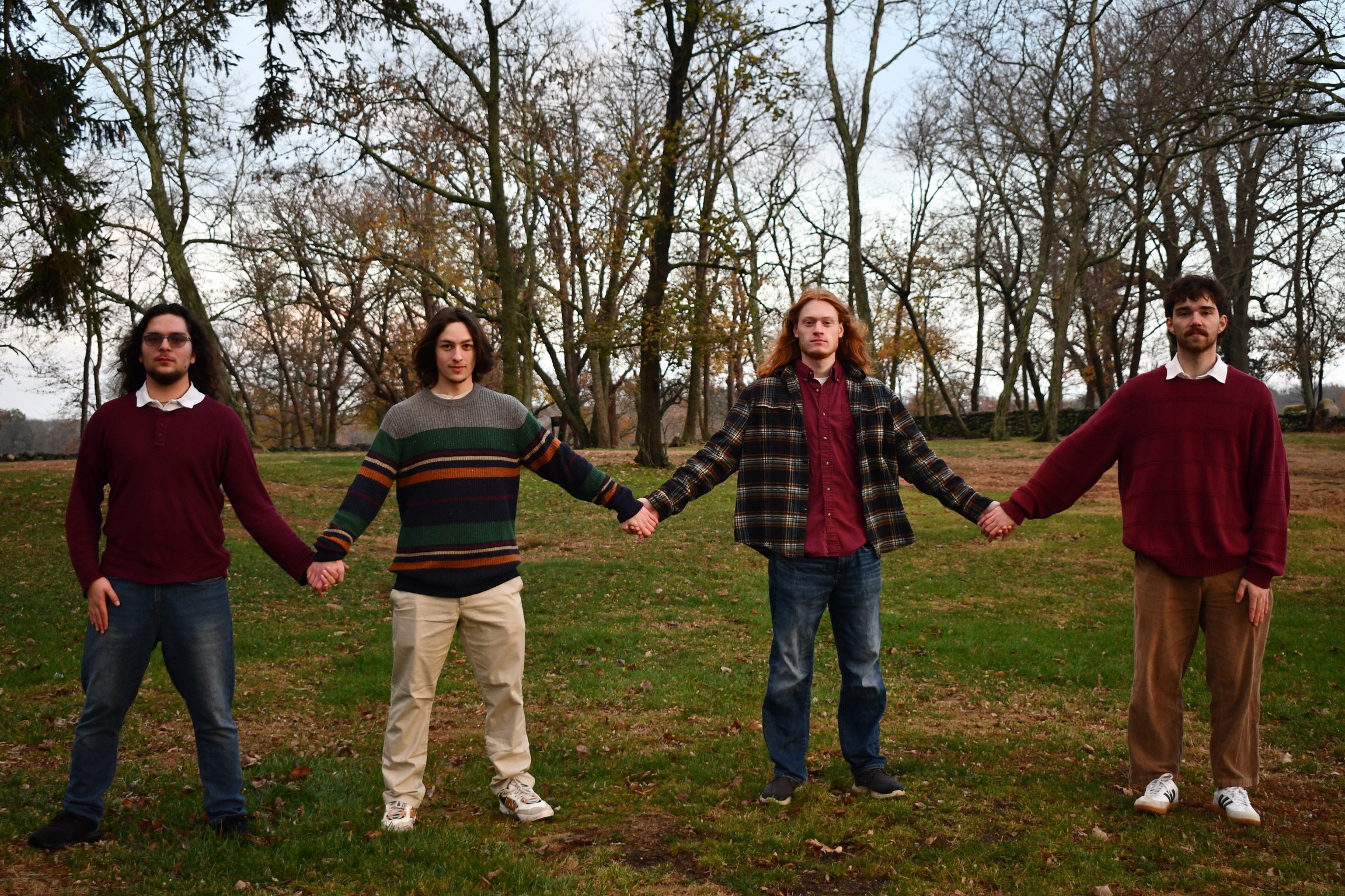 Maintenance standing outdoors in a park during fall, holding hands in a line across the grass with trees in the background.