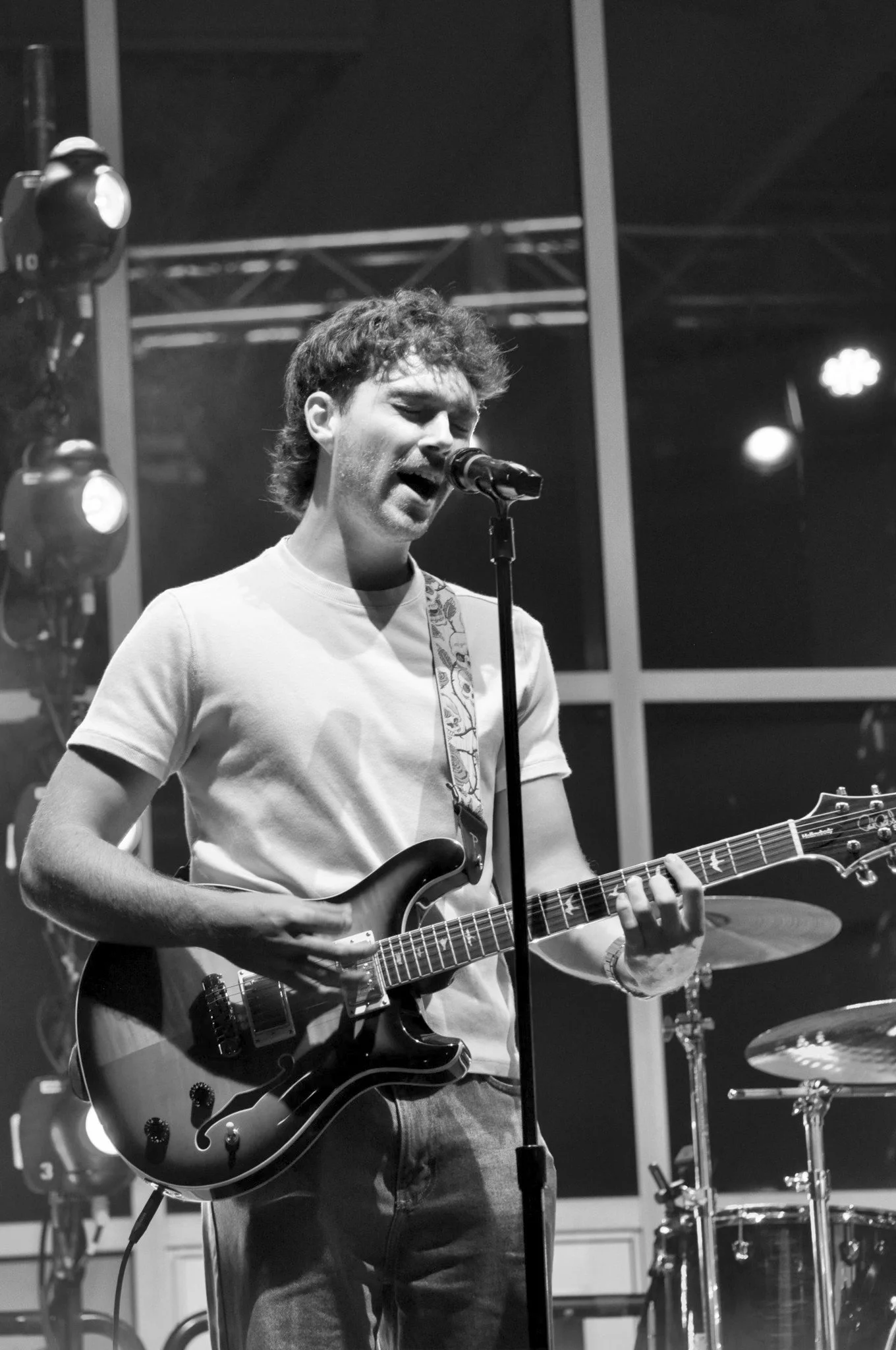 Nick singing into a microphone while playing an electric guitar on stage in black and white.