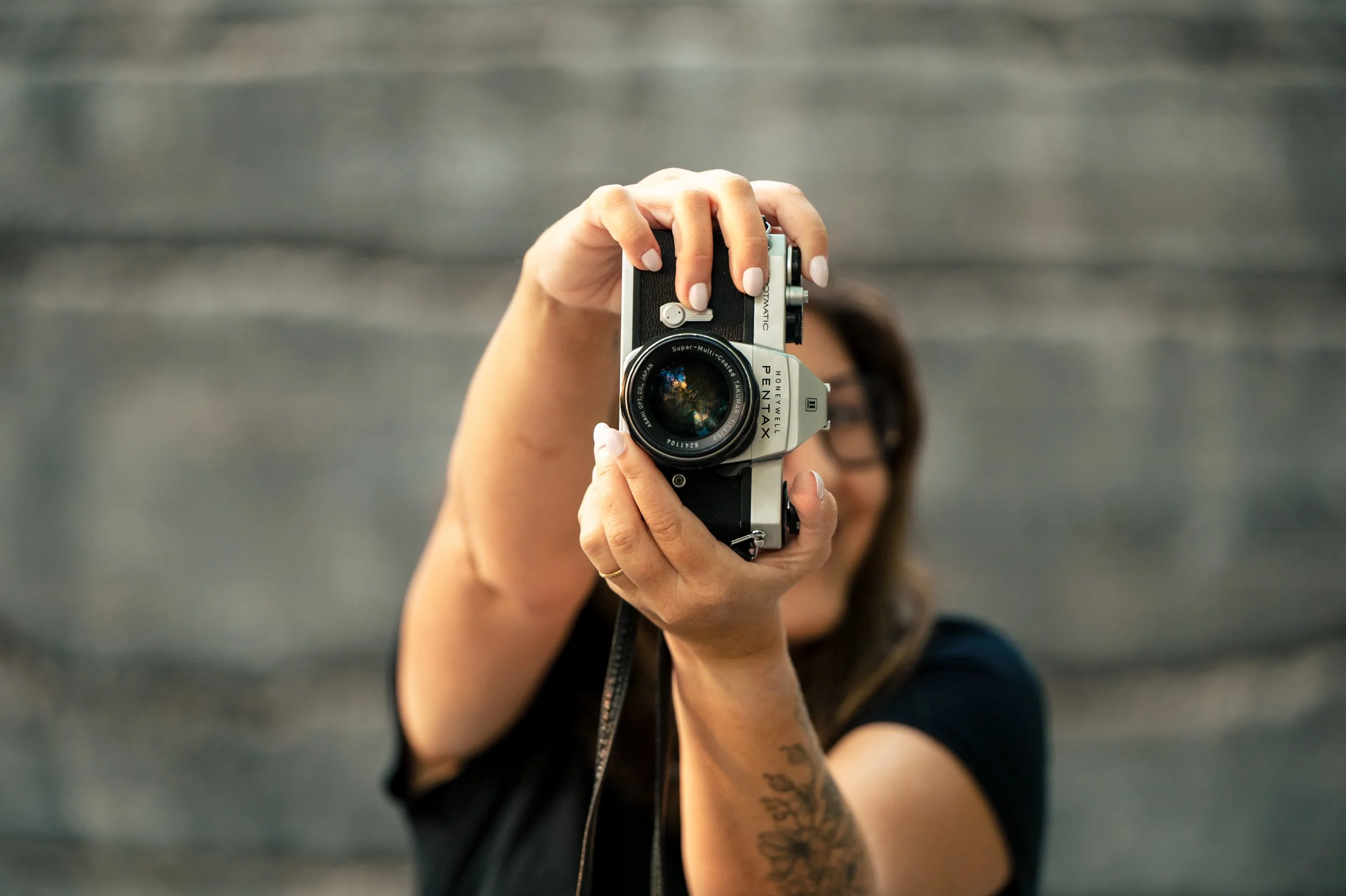 Person holding a vintage Pentax camera, taking a photo, with a blurred background.
