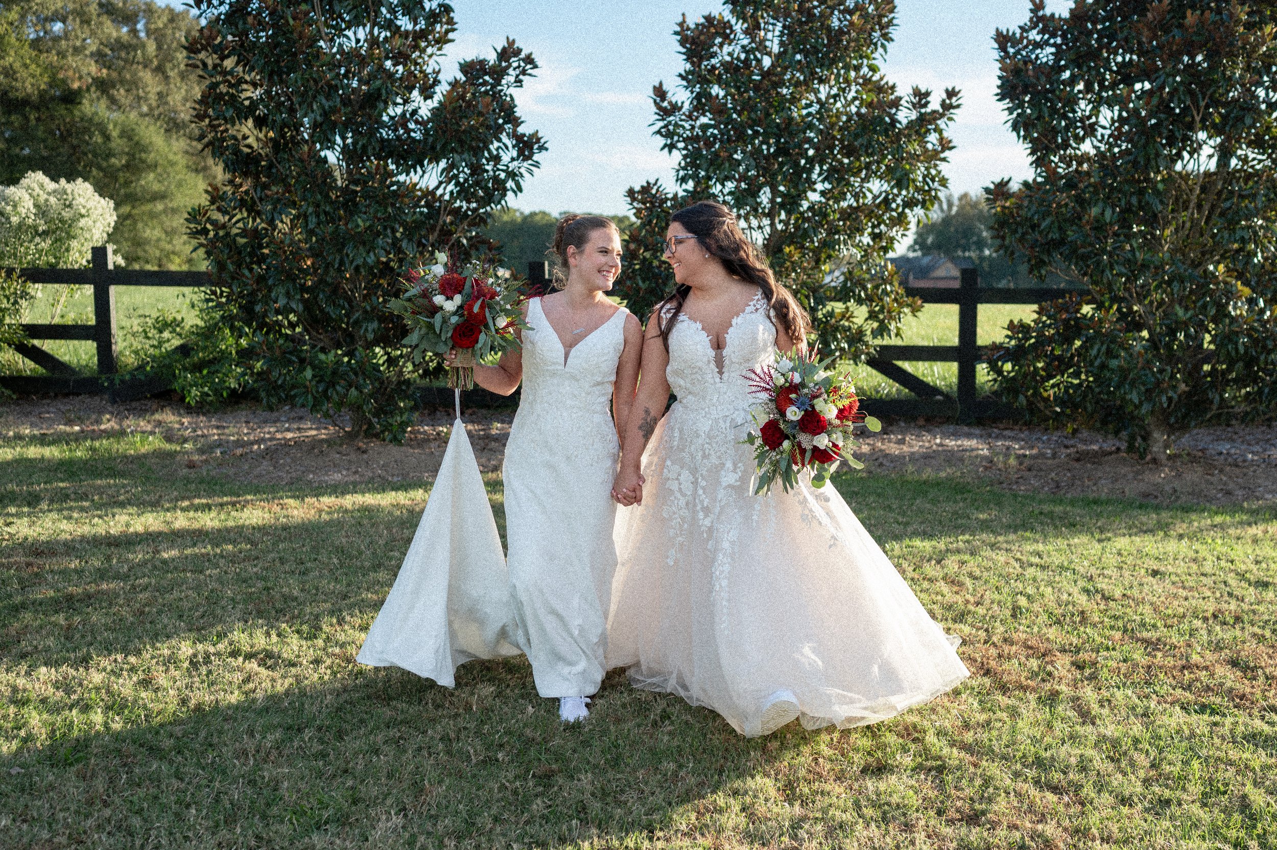 Laurie’s two brides walking hand in hand, farm wedding venuecustomers, Mariana and Carmen holding hands on a green lawn on their wedding day.