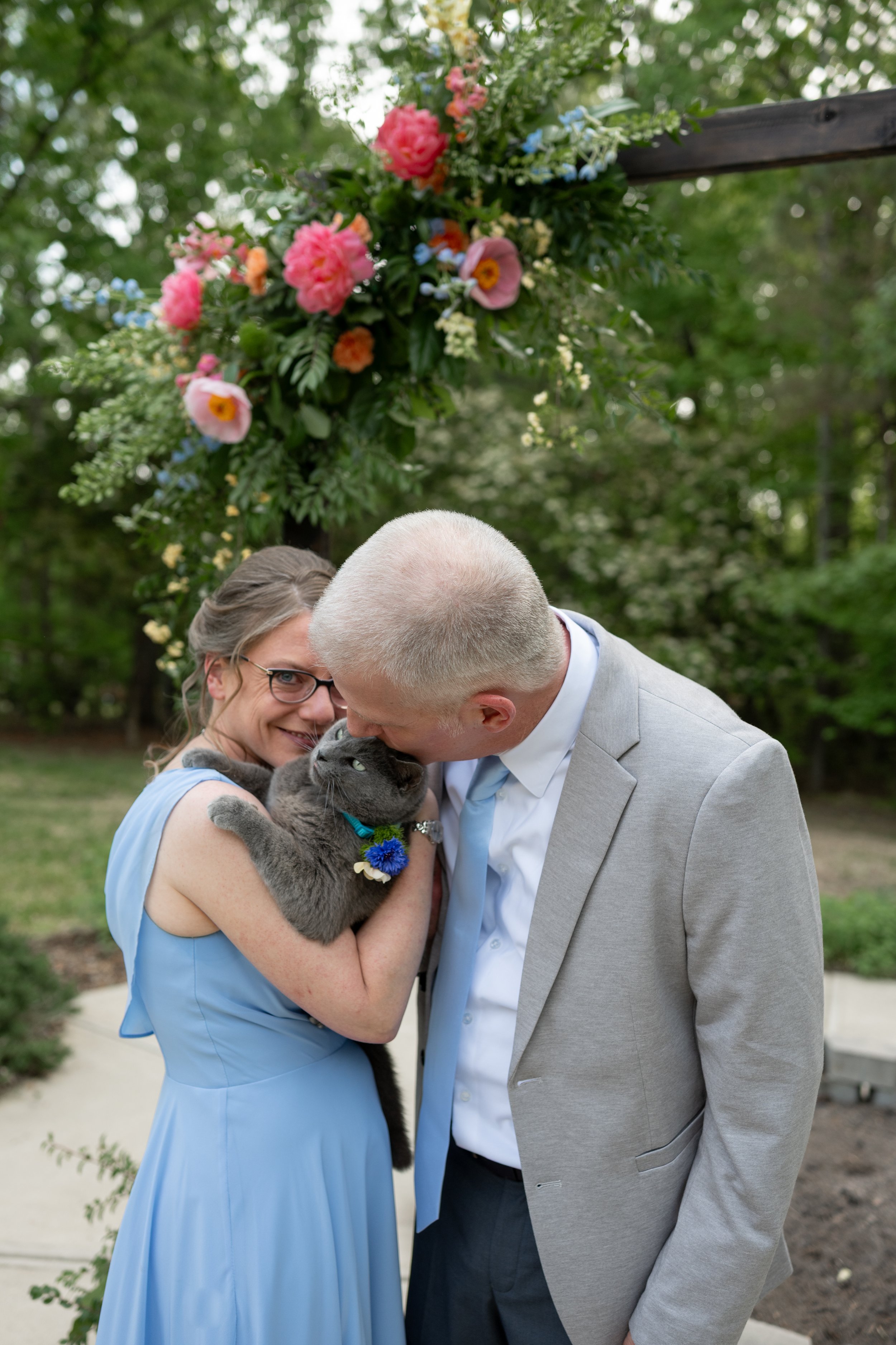 Wedding couple higging their gray cat by the ceremony arch
