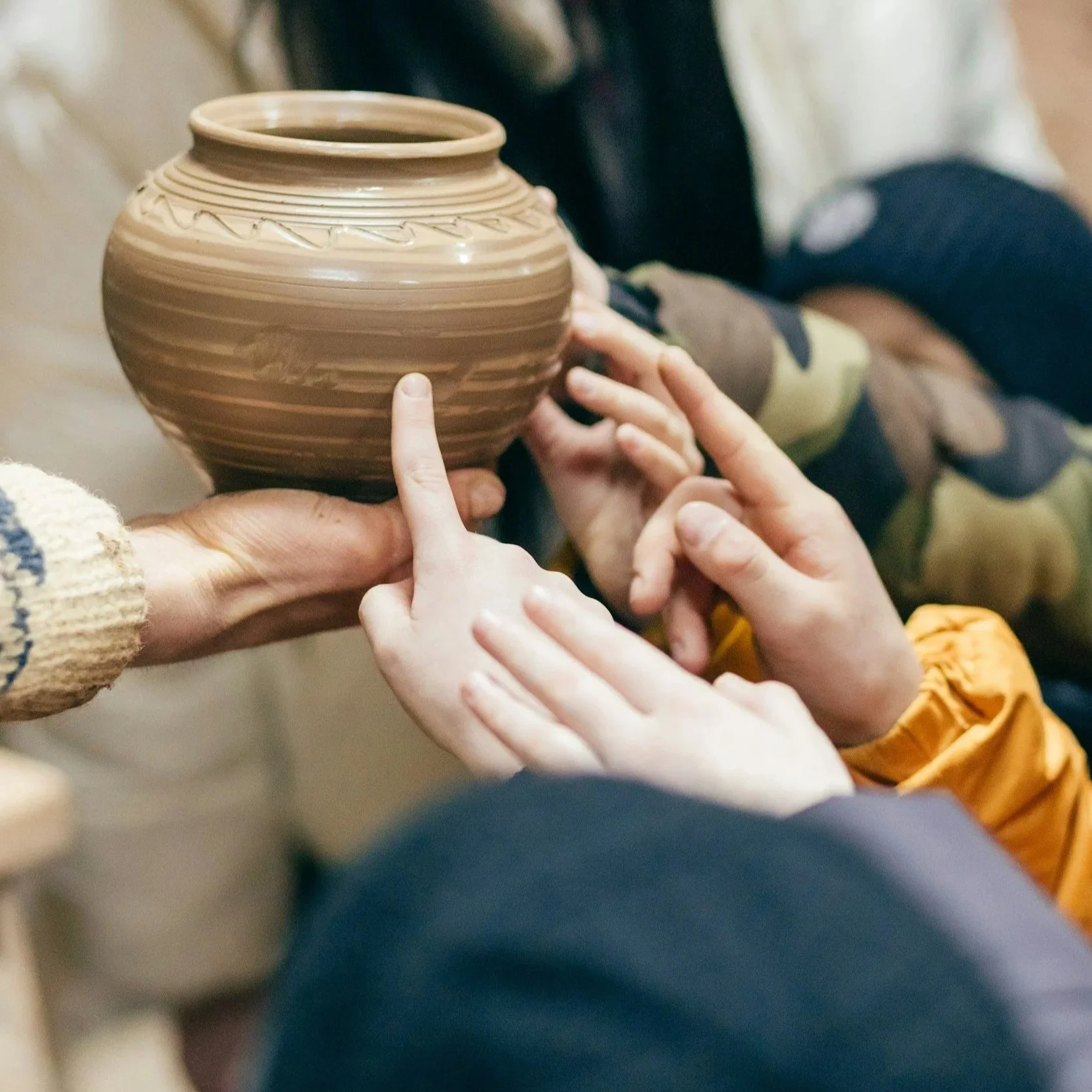 People examining a brown ceramic pot with layered patterns to see its texture and design.
