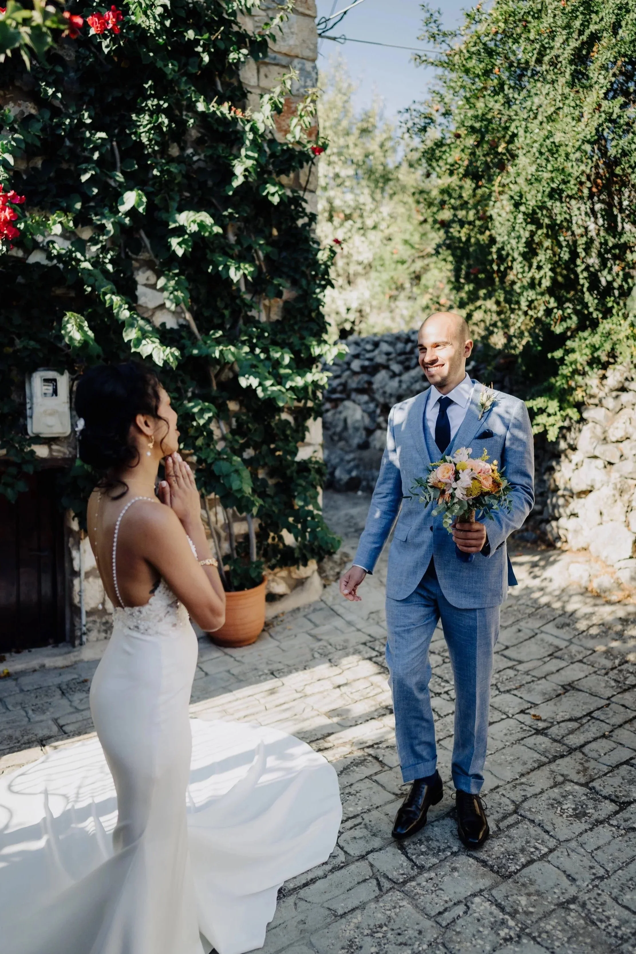 A bride and groom exchanging wedding vows outdoors surrounded by greenery and stone walls.