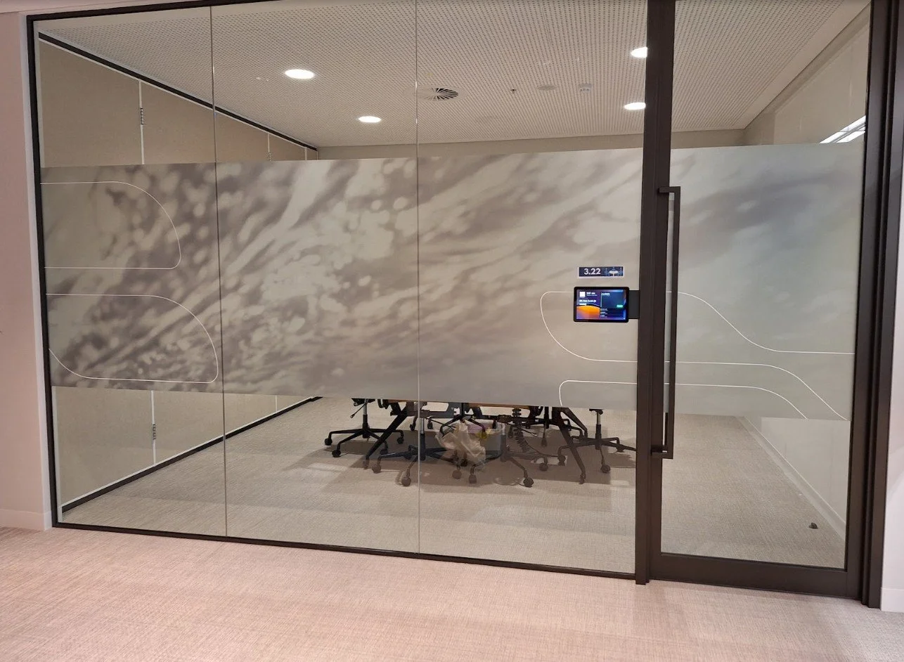 A large glass meeting room wall covered in a custom-printed film depicting a misty, abstract mountain landscape.