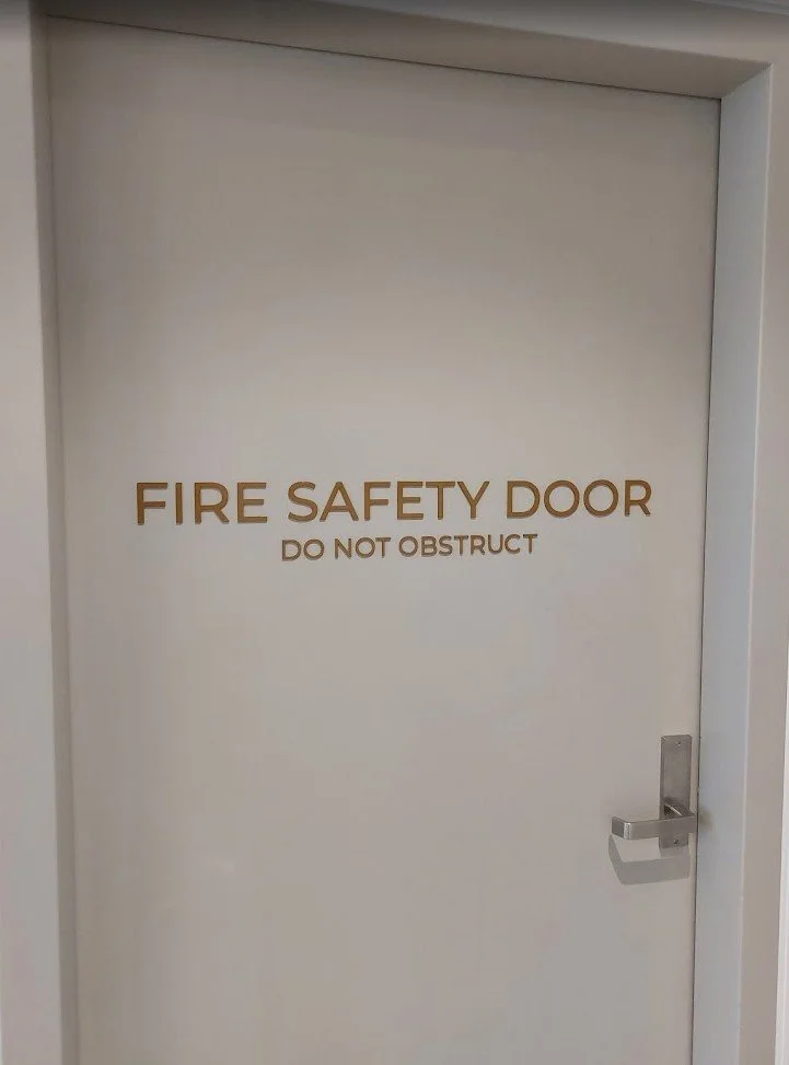 Professional fire safety door signage with laser cut out aluminium lettering installed in a commercial building.