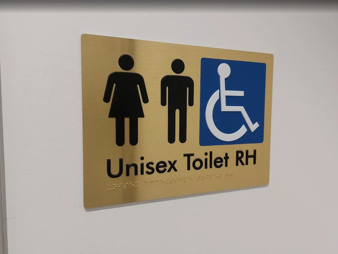Tactile gold braille toilet compliance sign for accessible amenities, professionally wall-mounted.