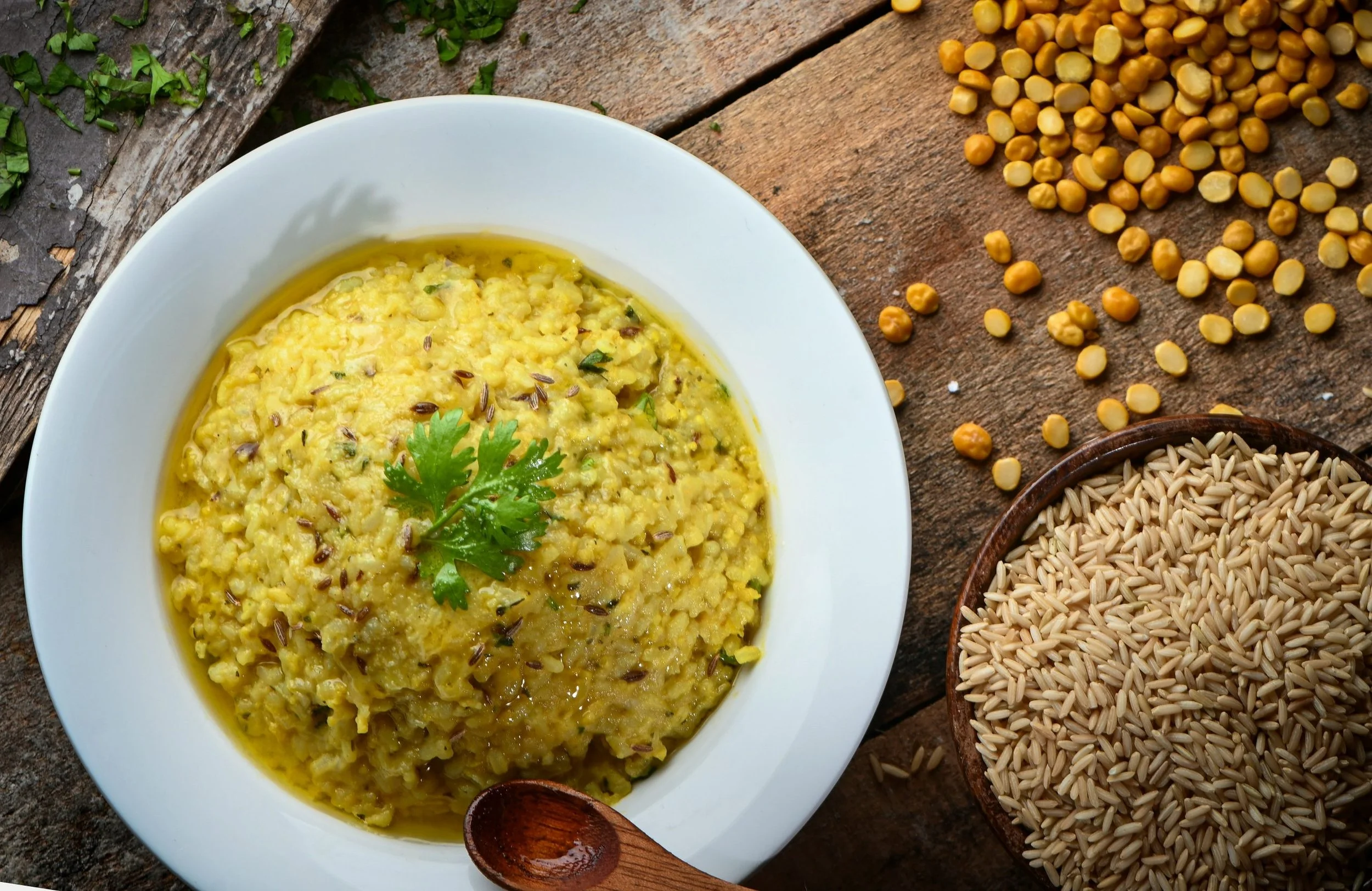 Bowl of yellow mung dal kitchari beside uncooked basmati rice and split mung beans
