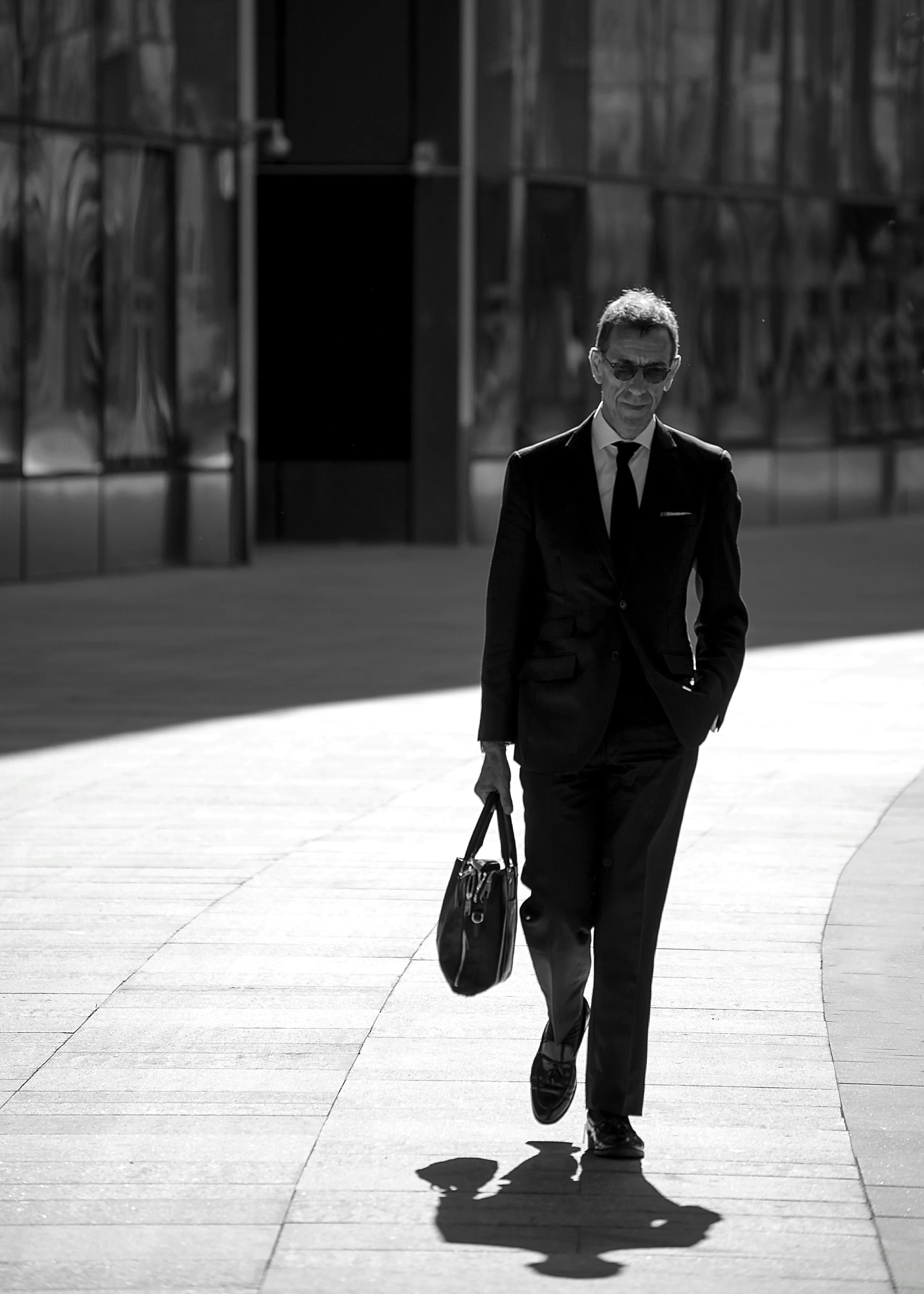  Black and white image of a well dressed man walking on a concrete path holding a briefcase - Ospan Ali Unsplash 