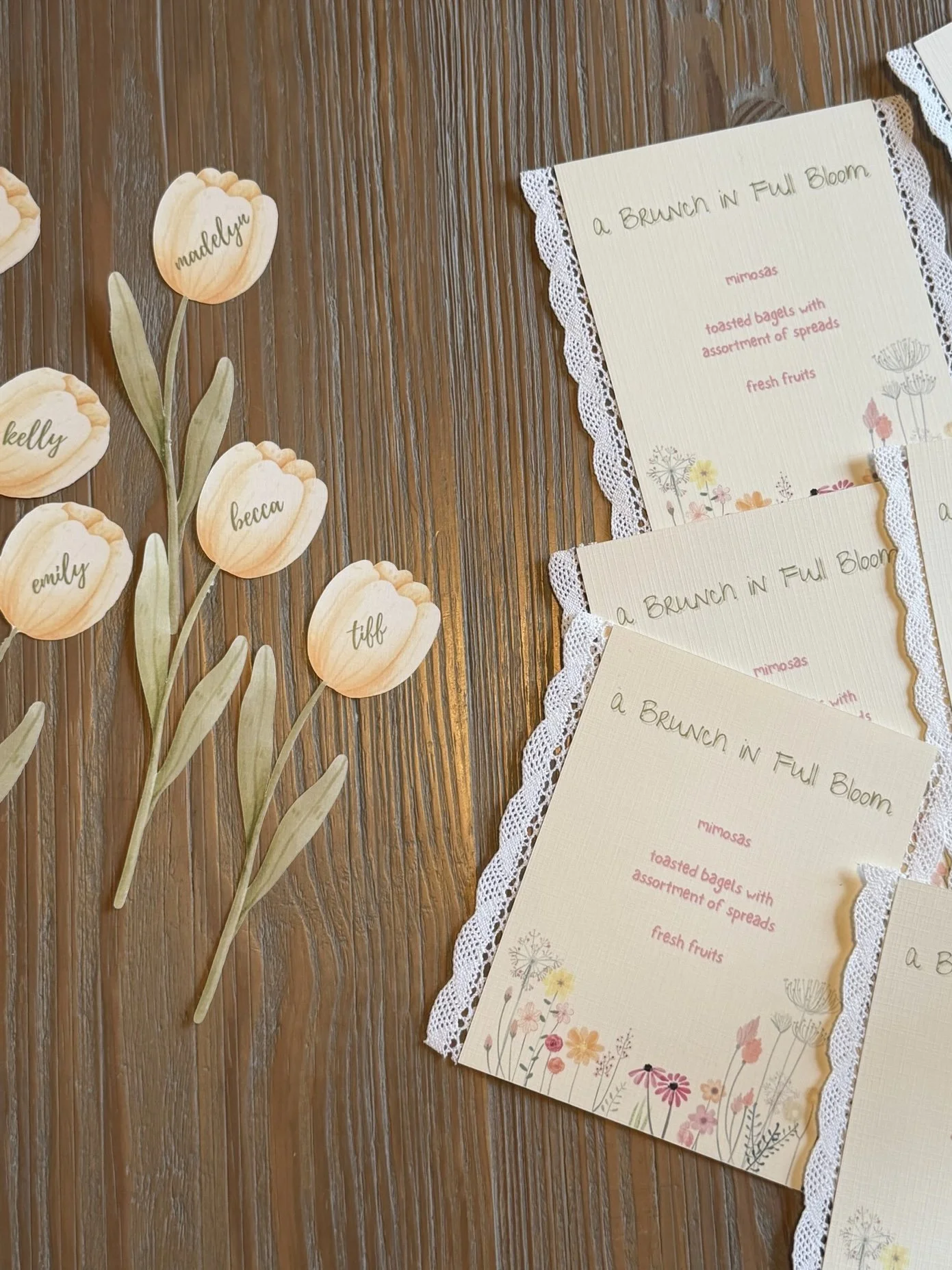 Decorative place cards with floral designs and food menu cards on a wooden table.