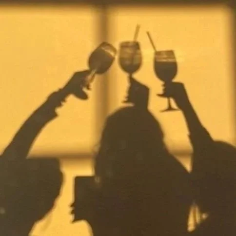 Silhouettes of three people holding up drinks against a yellow background.