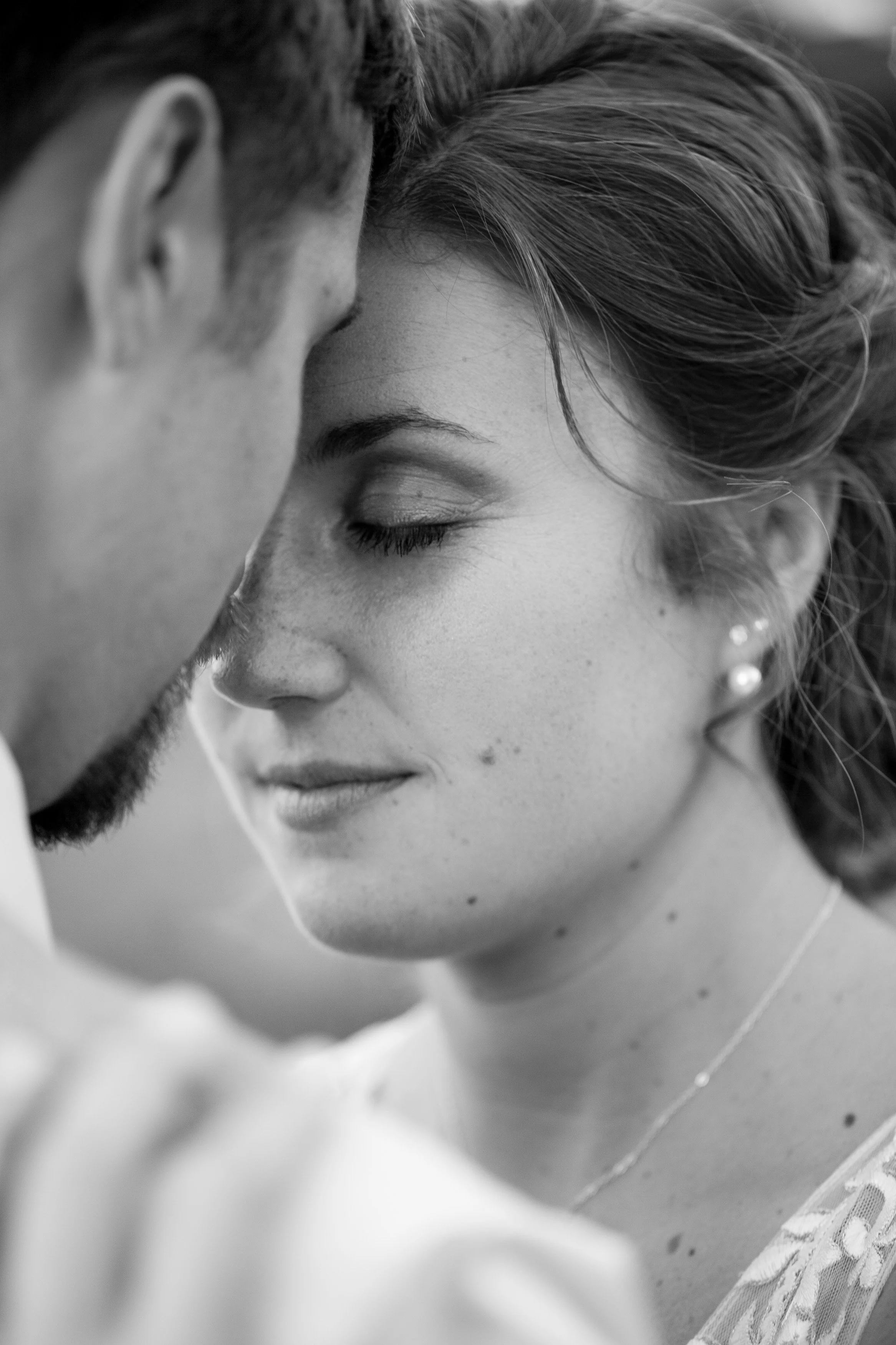 A black and white close-up photo of a couple touching foreheads with eyes closed, expressing intimacy and affection.