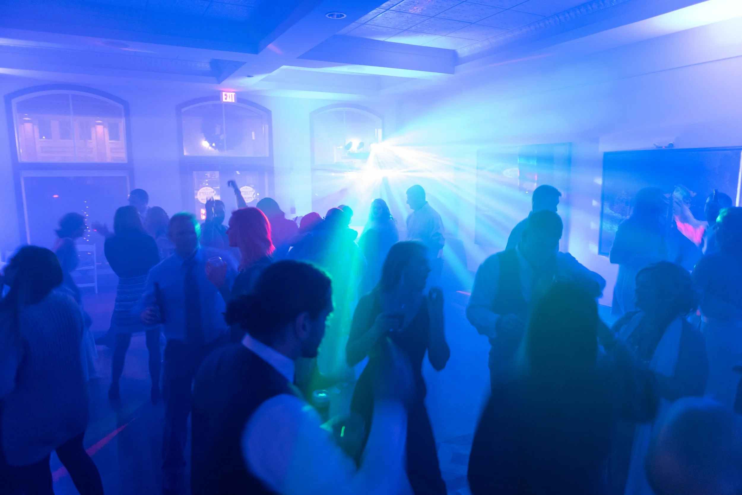 People dancing at a party with colorful lights and a light show in a dimly lit room.