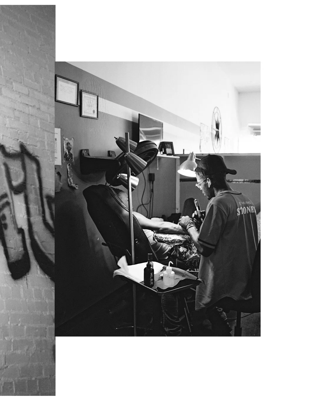 A tattoo artist working on a client's arm in a tattoo shop, with tattoo supplies on a nearby table.