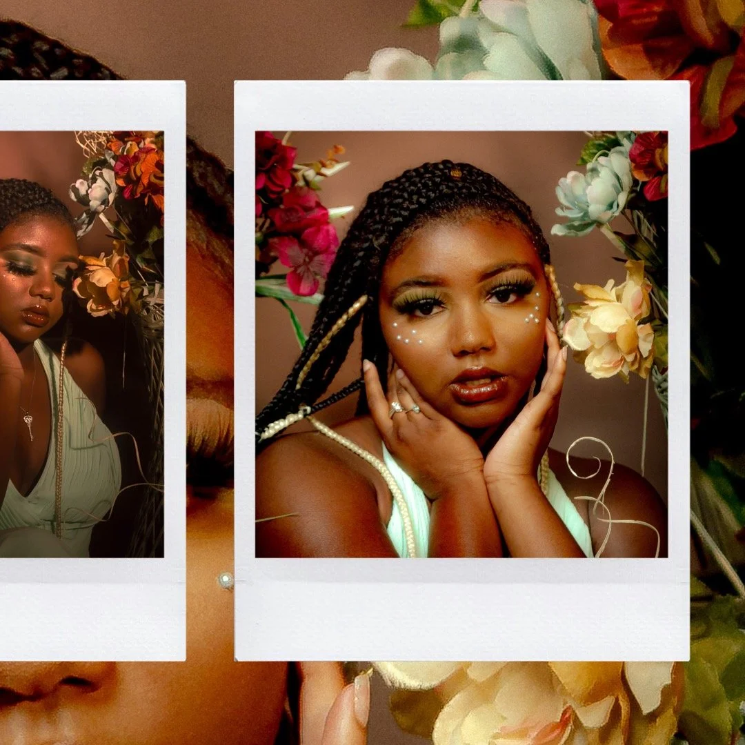 A woman with braided hair and makeup adorned with small white gems posing with her hands on her face surrounded by colorful flowers.