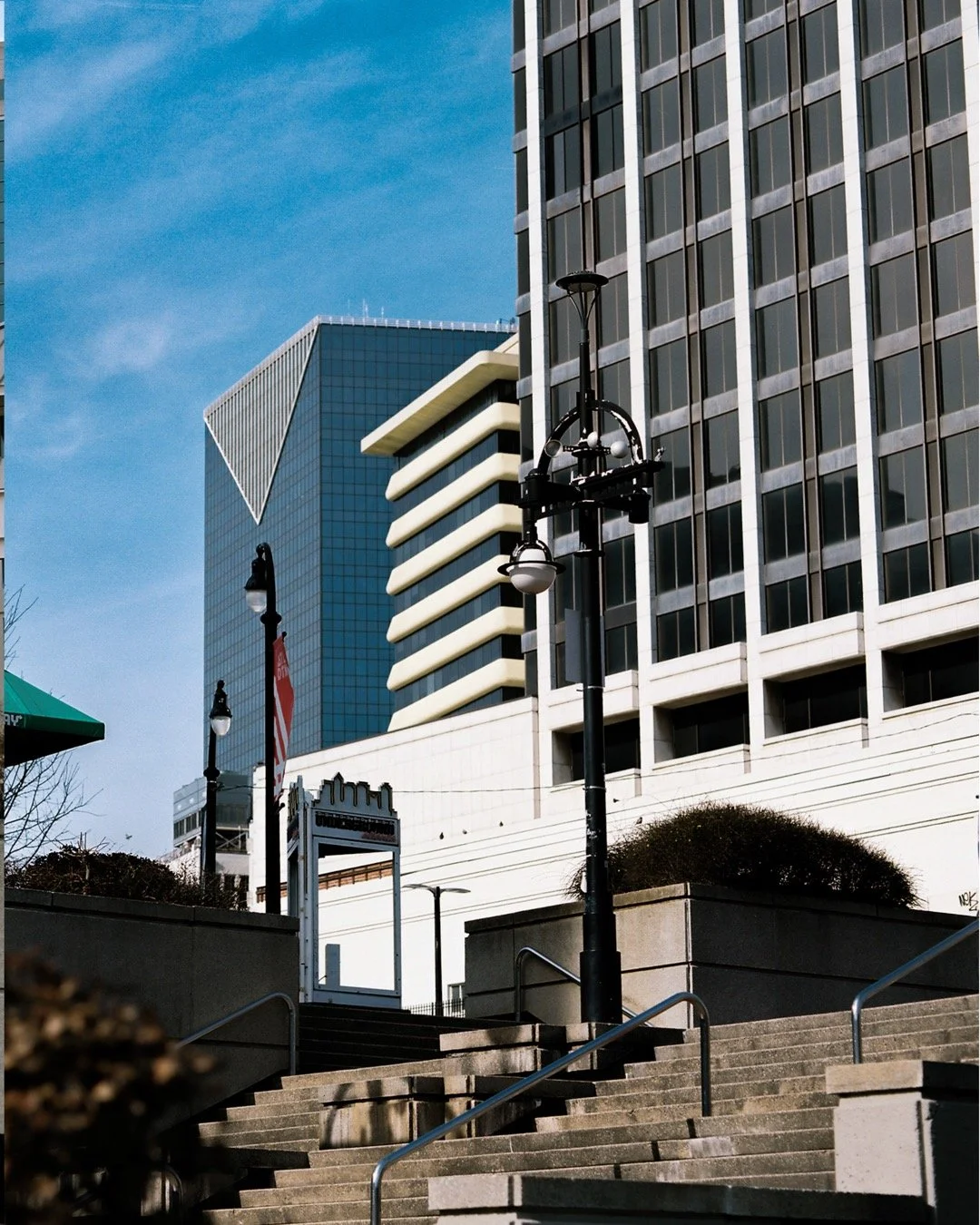 Cityscape with tall modern office buildings, staircases, lamp posts, and clear blue sky.