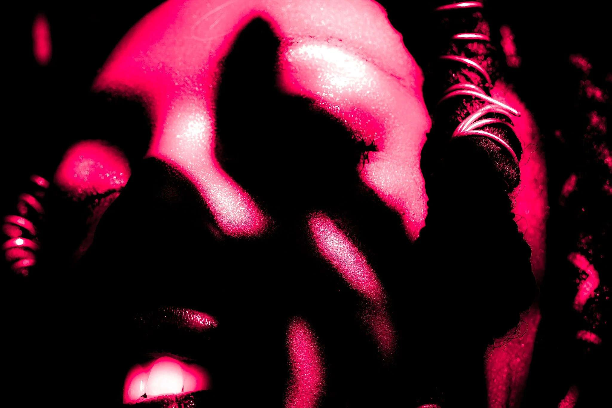 Close-up of a face with makeup, illuminated in pink and black, with metallic spiral accessories around the head.