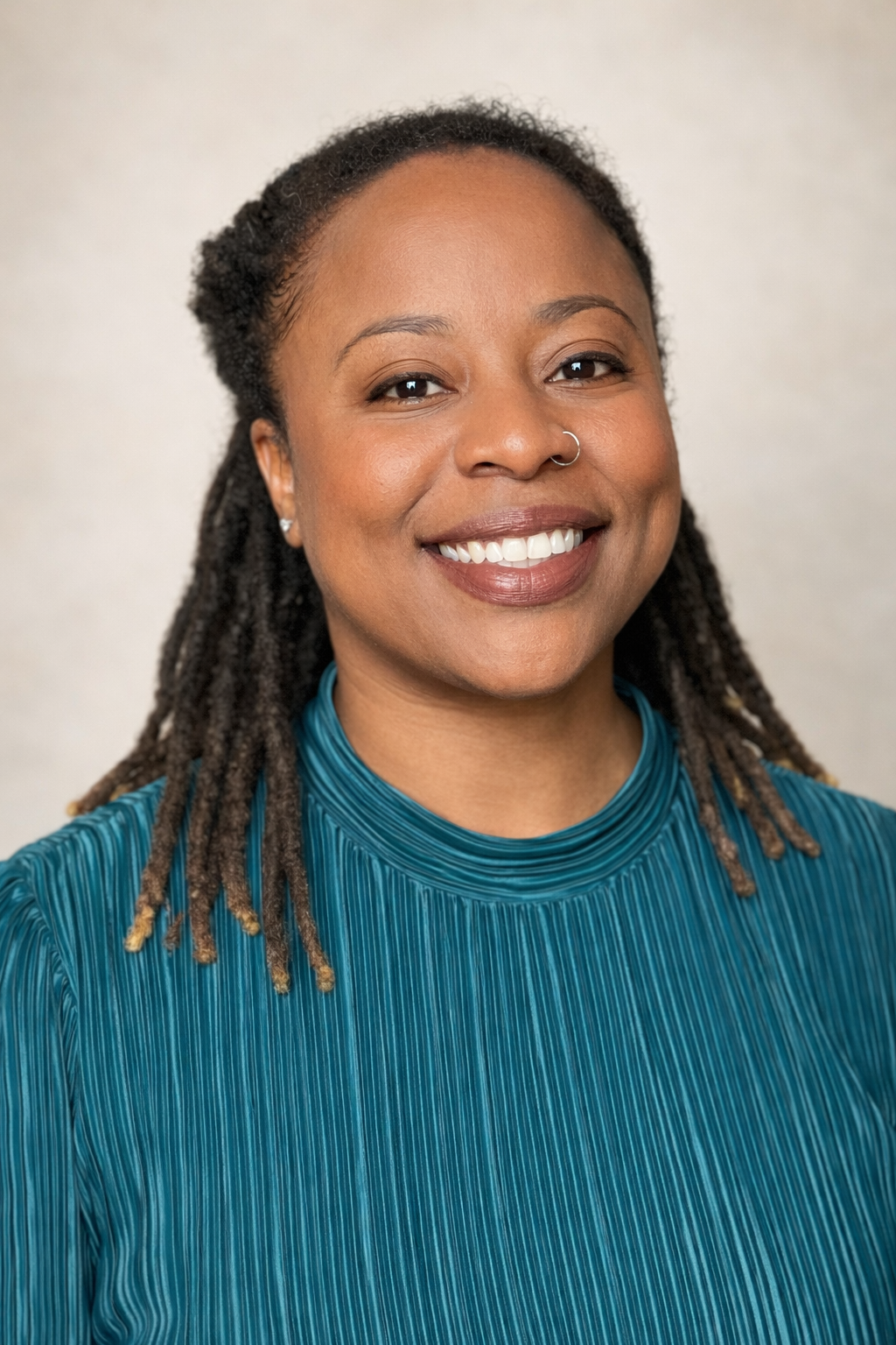 A woman with dreadlocks wearing a teal pleated top, smiling at the camera.