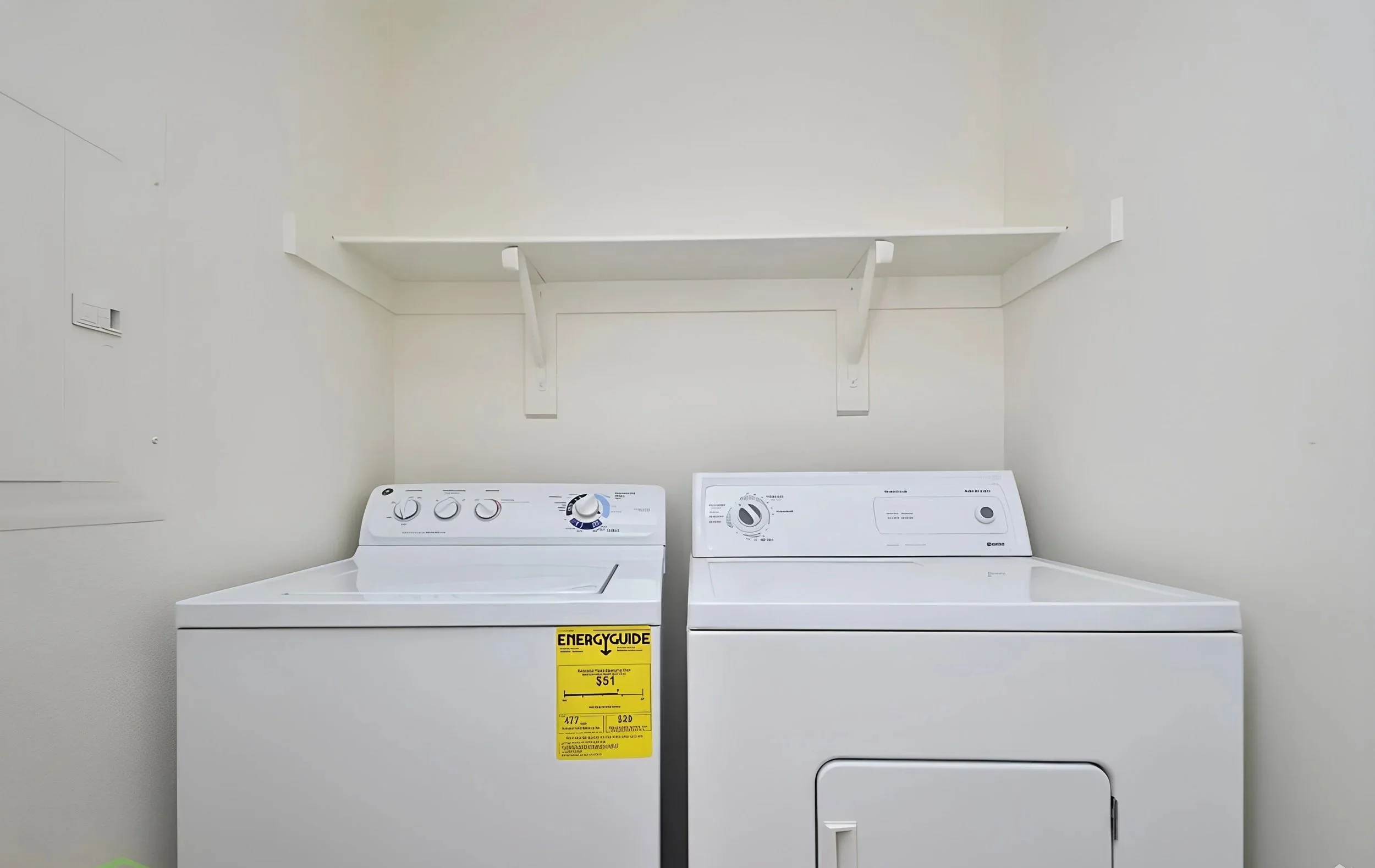 White washing machine and dryer in a laundry room with a white shelf above them.