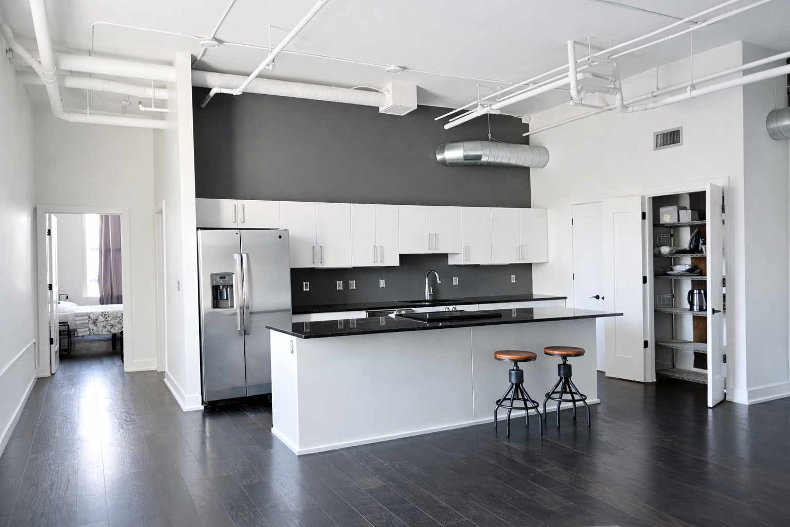 Modern kitchen with white cabinets, black granite countertops, stainless steel refrigerator, and two bar stools with wooden seats next to the island.
