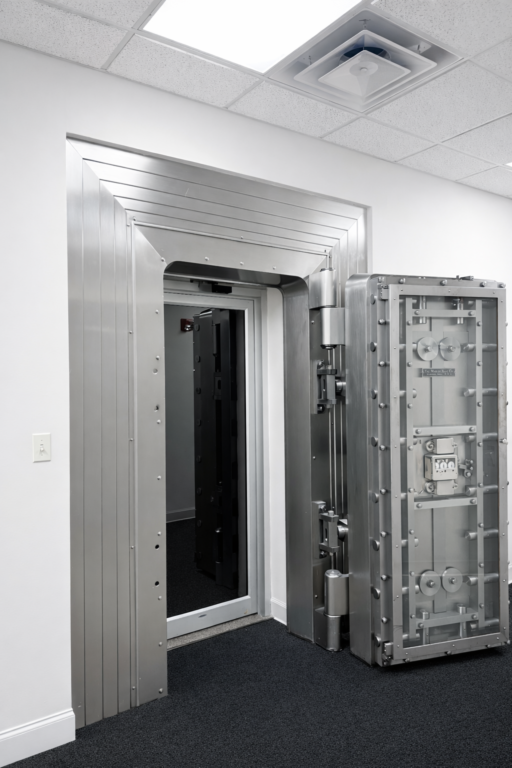 A large, advanced steel safe with an open door, located in a modern white-walled room with a drop ceiling and a vent.