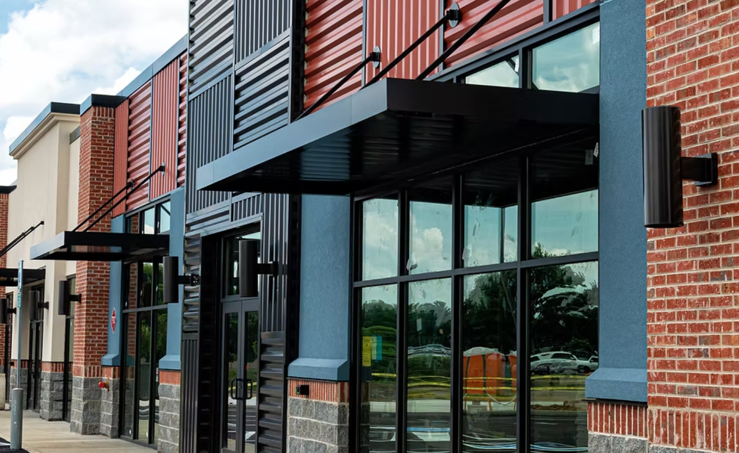 Modern commercial building with brick and metal siding, large glass windows, and black awnings.