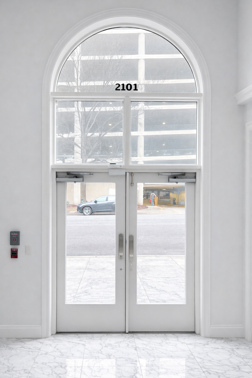 Entrance door with glass panels above a marble floor, with a building and parked car outside, and the number 2101 displayed above.
