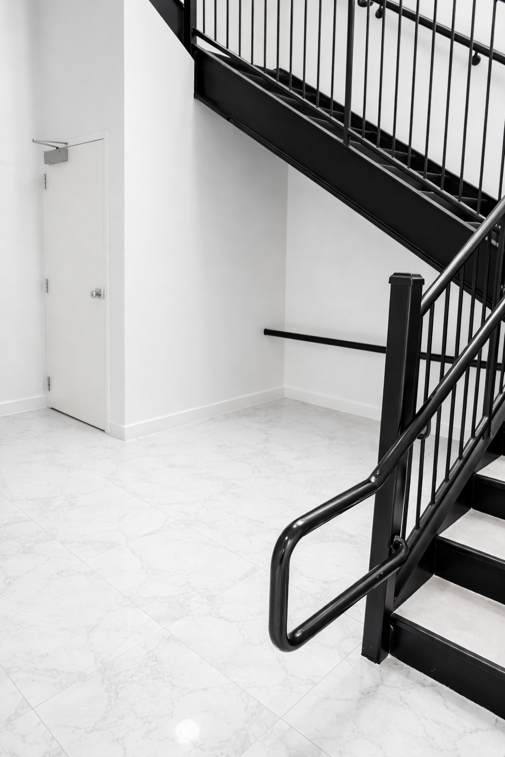Interior view of a stairwell with white marble floor, white walls, a closed white door, and black metal stair railings.