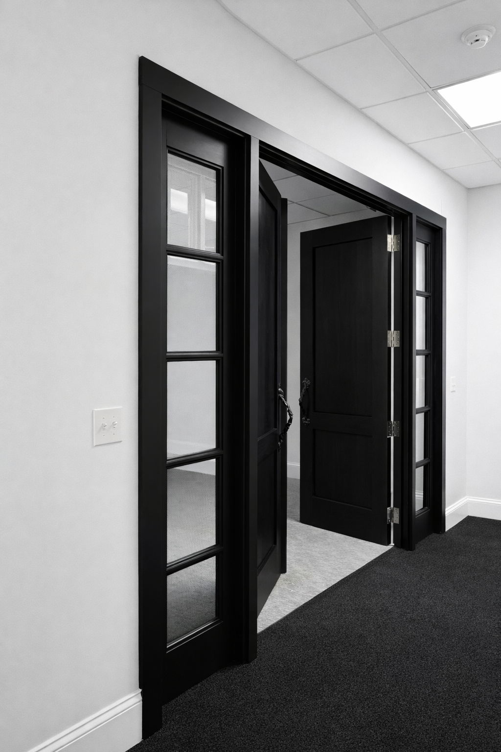 Open black double glass-paned doors in a modern office with white walls and black carpet.