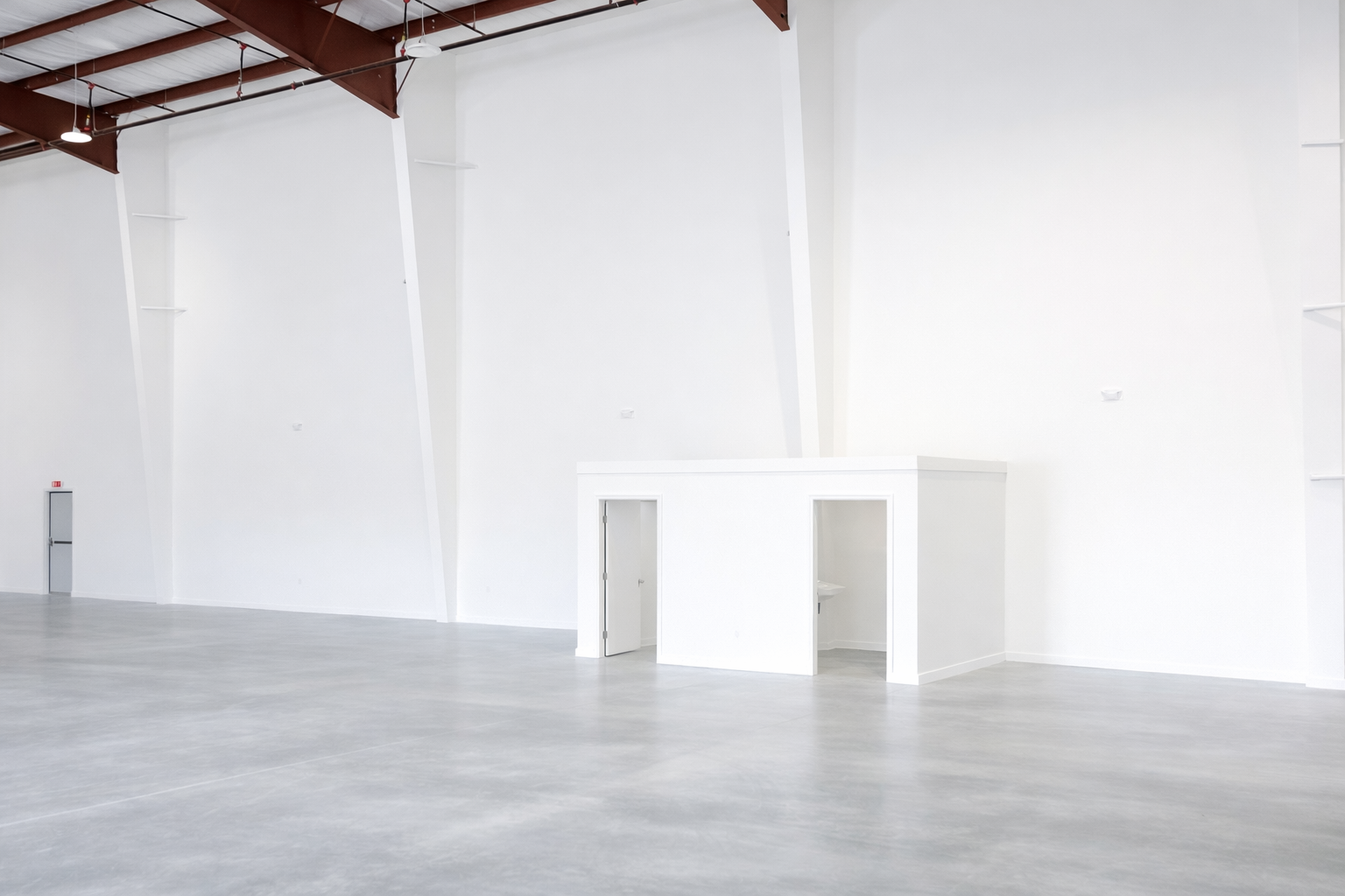 Empty white gallery or event space with high ceilings, exposed beams, and a small white booth or station at the front
