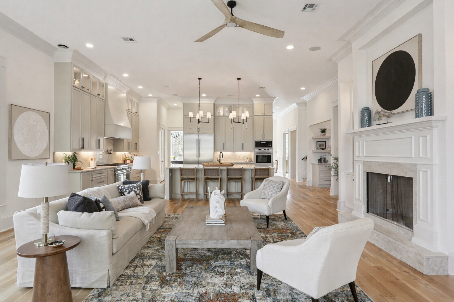 Open concept living room and kitchen in a modern home with light-colored walls, hardwood floors, a fireplace, and minimalist decor.