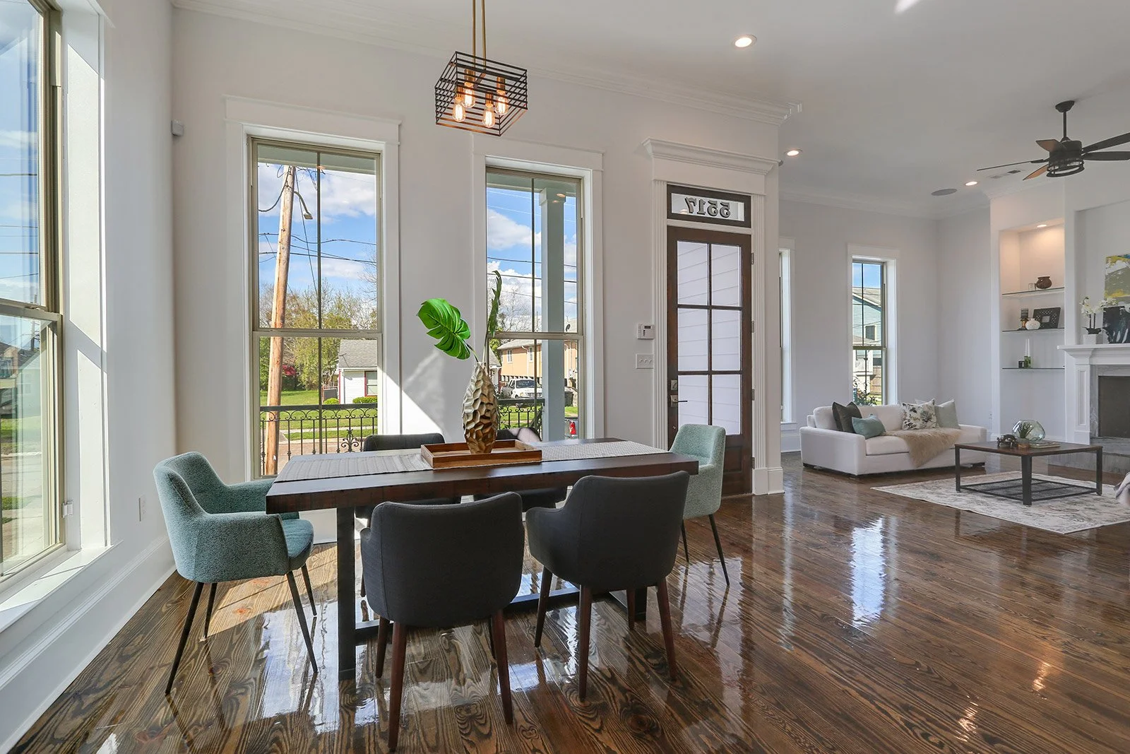 Interior of a bright, spacious living and dining area with hardwood floors, twelve foot ceilings, white walls, large windows, and modern furniture, including a dining table with chairs and a white sofa with cushions.