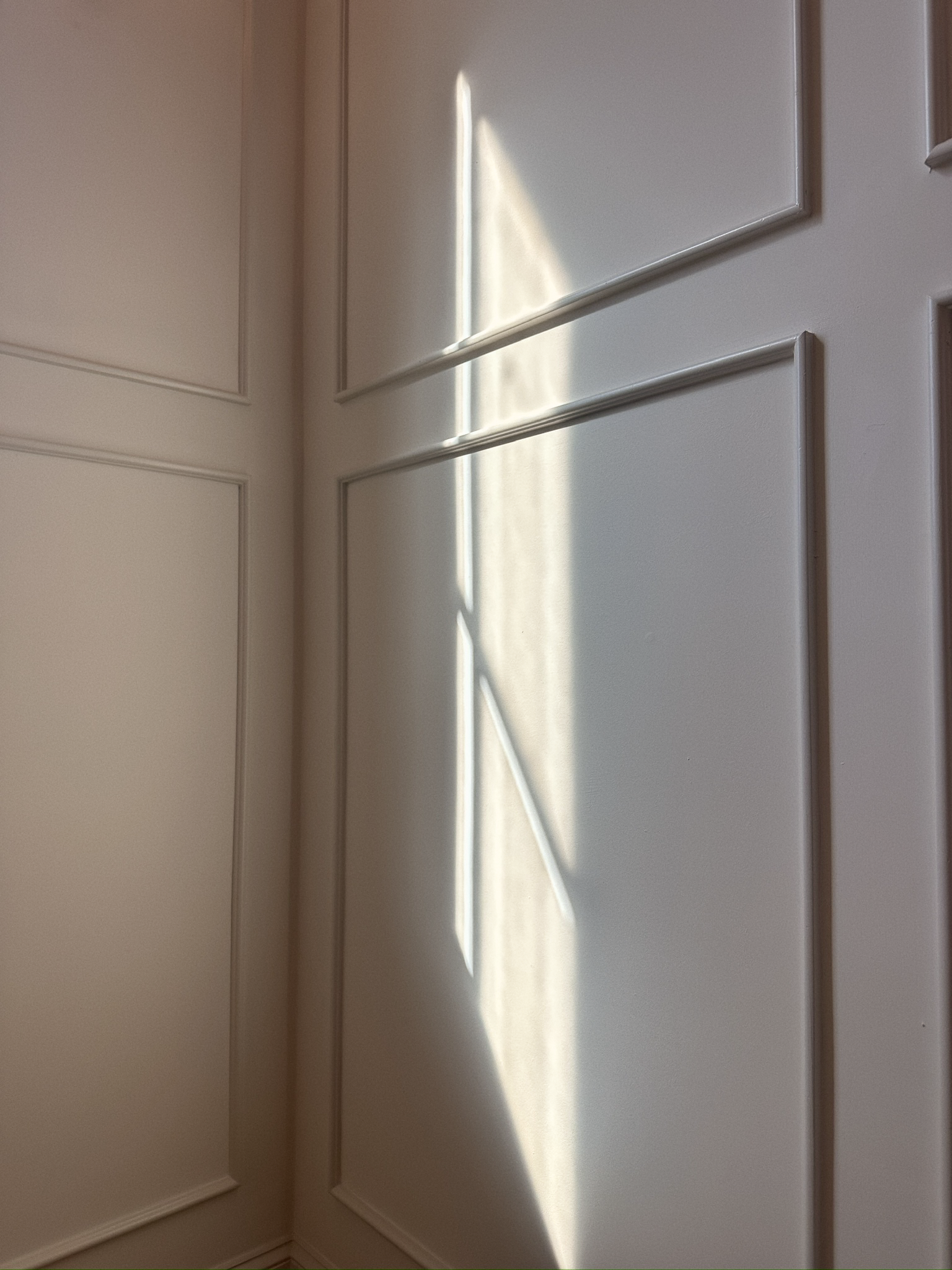 Sunlight shining through a window onto a white paneled door, creating geometric shadows.